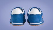 Pair of blue and white sneakers with gum soles shown from the back on a purple background.