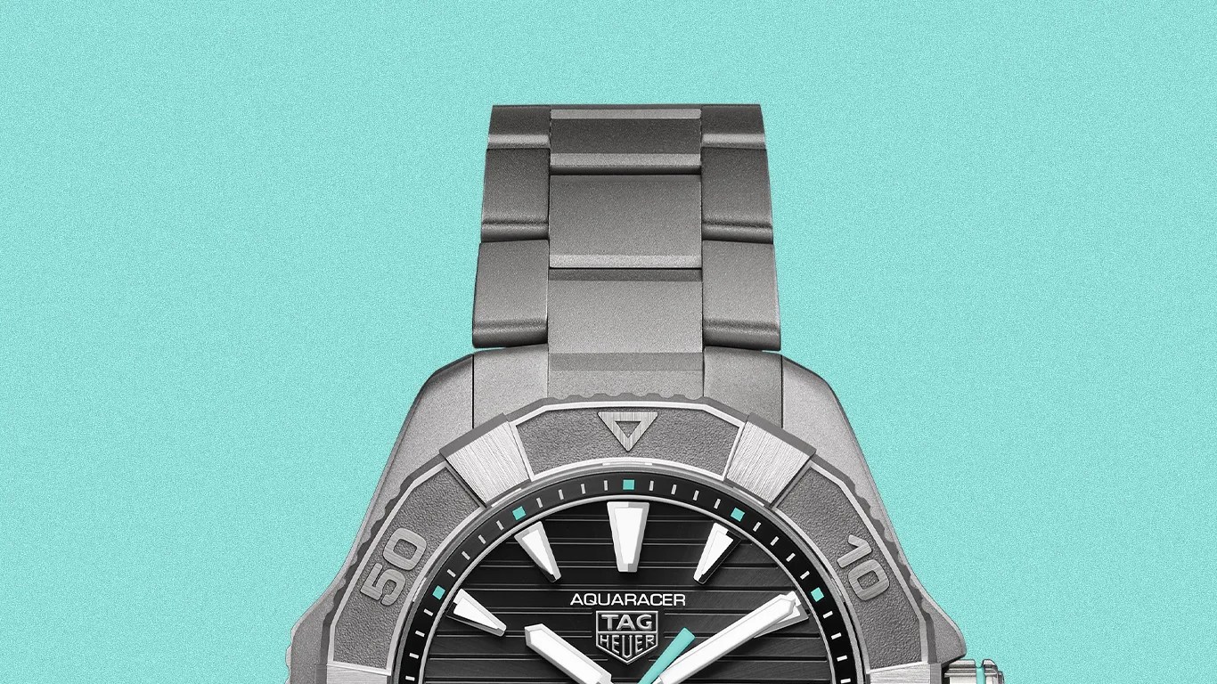 TAG Heuer Aquaracer watch with black striped dial, silver-tone hands, and stainless steel bracelet on turquoise background.