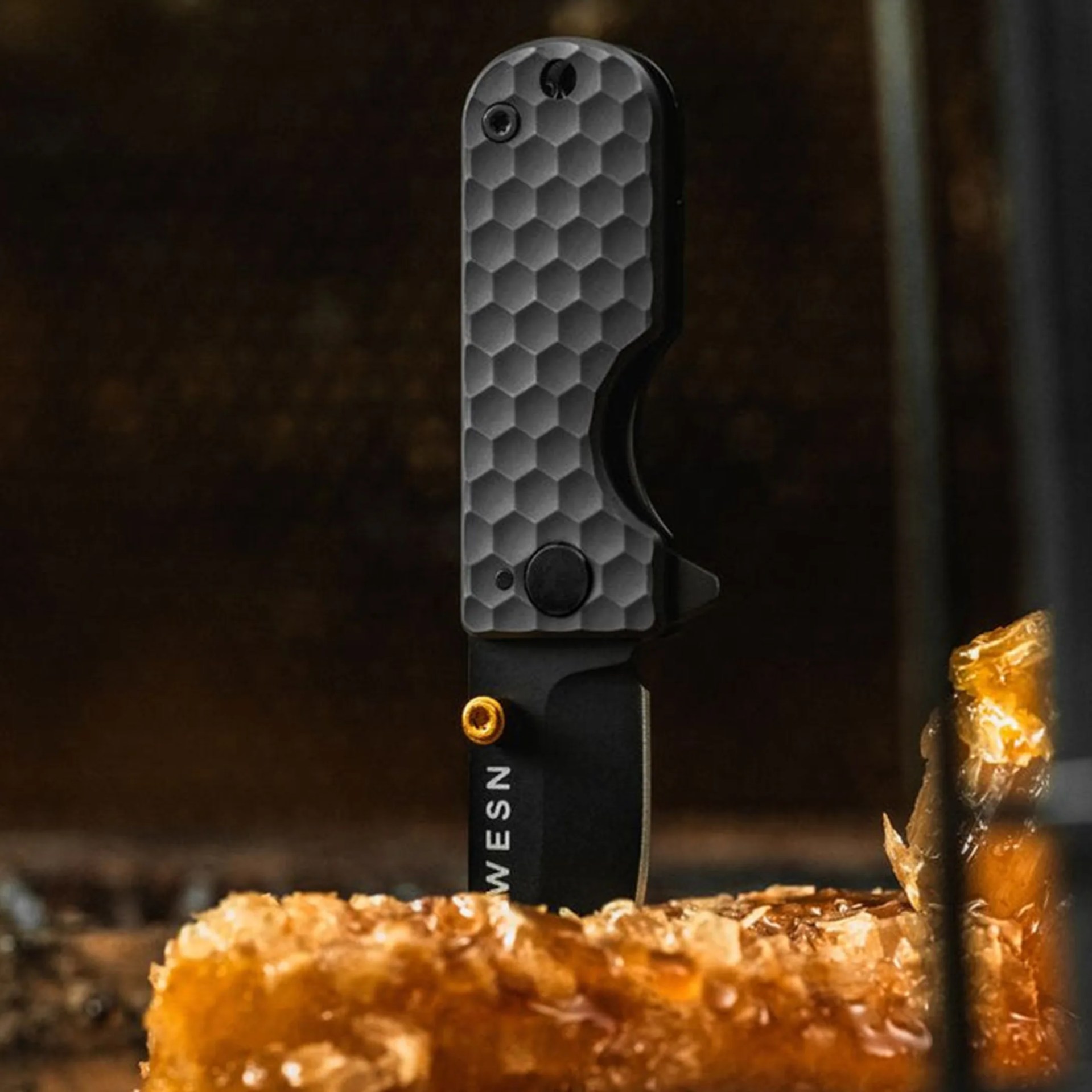 Black folding knife with a honeycomb textured handle stabbed into a piece of crispy fried food.