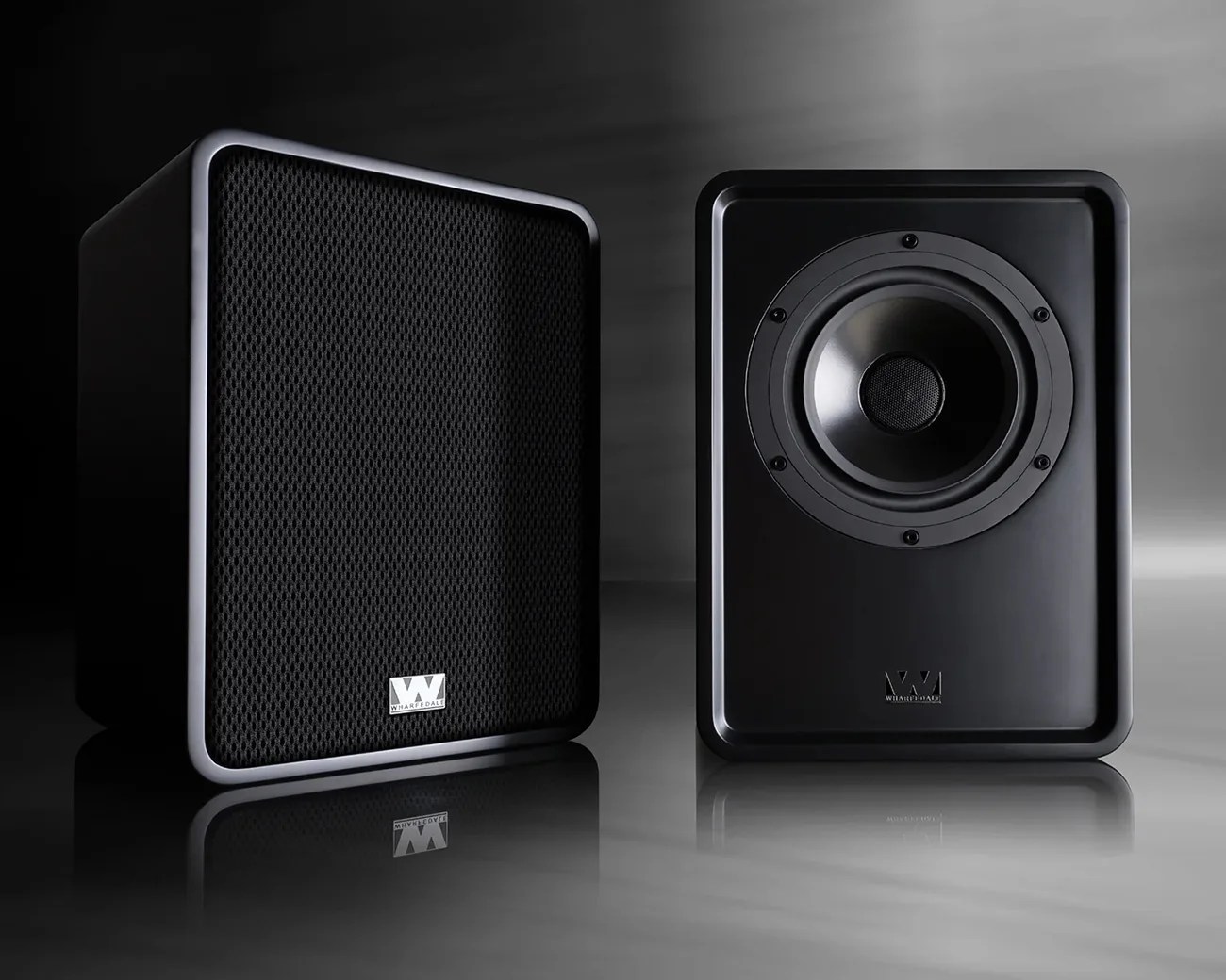 Pair of black Wharfedale speakers, one with mesh grille and one showing the woofer, on a reflective surface.