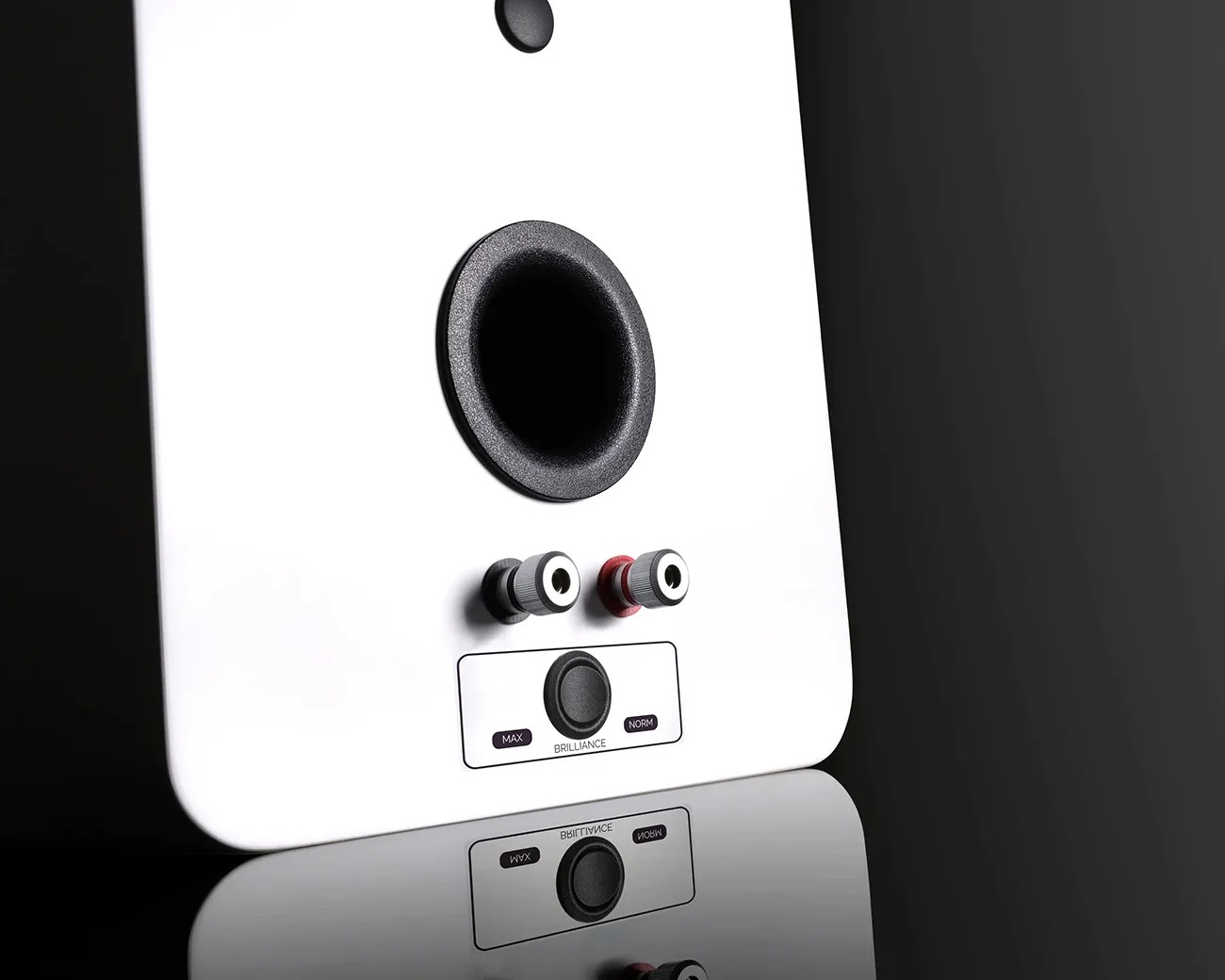 Close-up of the back of a white speaker with a circular port, two speaker wire terminals, and a brilliance control knob.