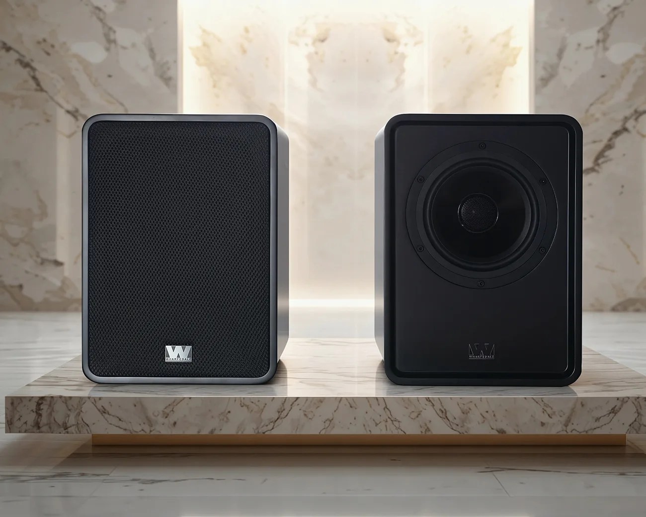 Pair of black Wharfedale bookshelf speakers on a polished marble surface with one speaker grille on and the other off.