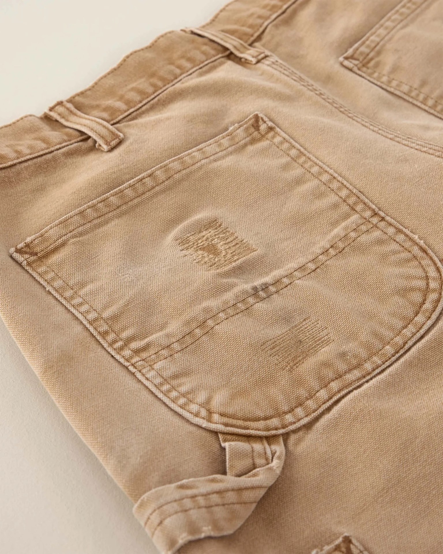 Close-up of a beige denim pocket with visible stitching and slight distressed details.