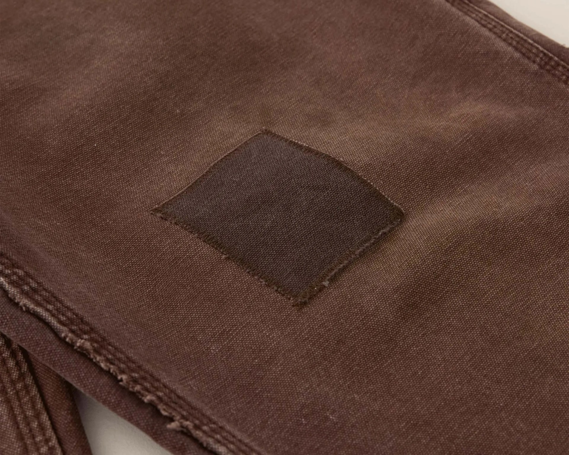 Brown fabric with a darker brown square patch sewn on and visible stitching along the edges.