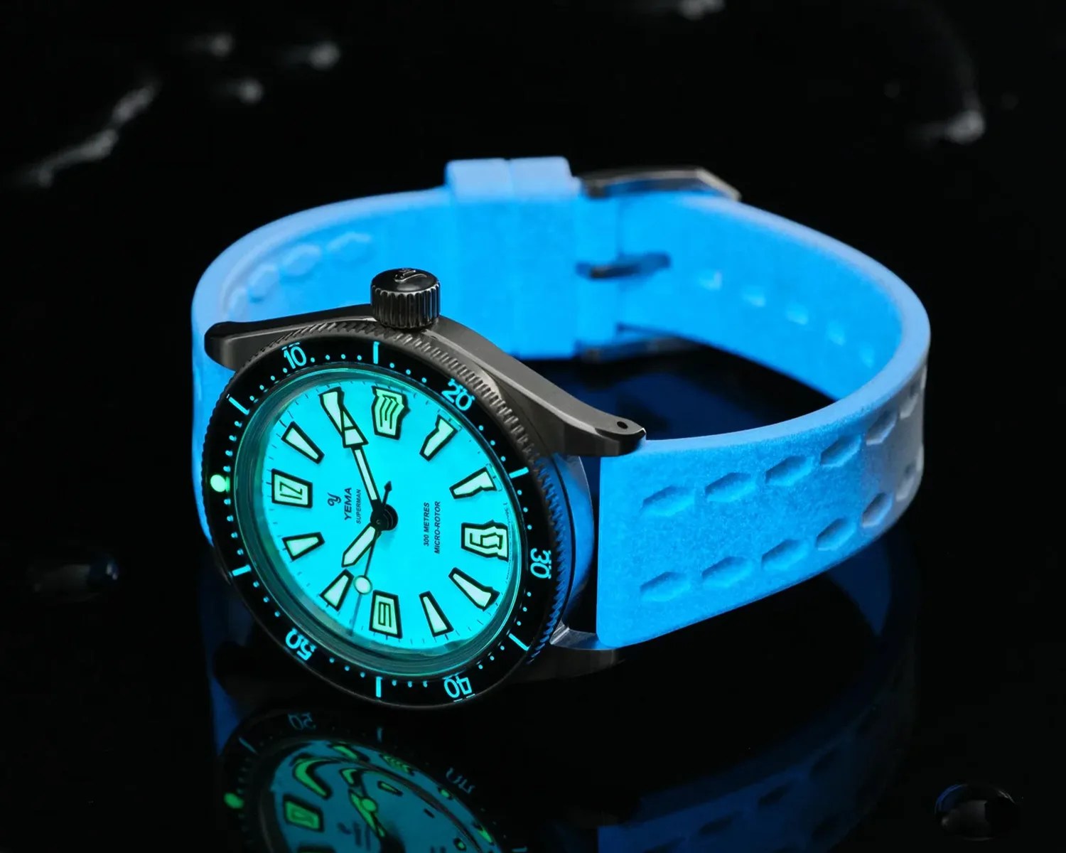 Steel dive watch with glowing blue dial and blue textured silicone strap on a reflective black surface.