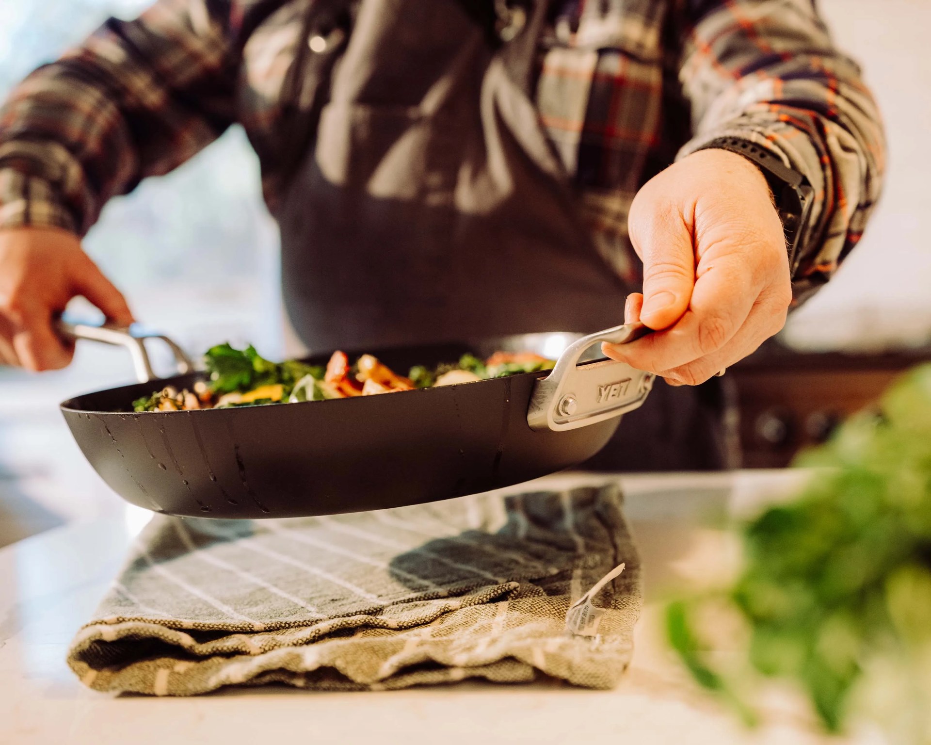 Person holding a black YETI frying pan with cooked vegetables inside over a kitchen counter.