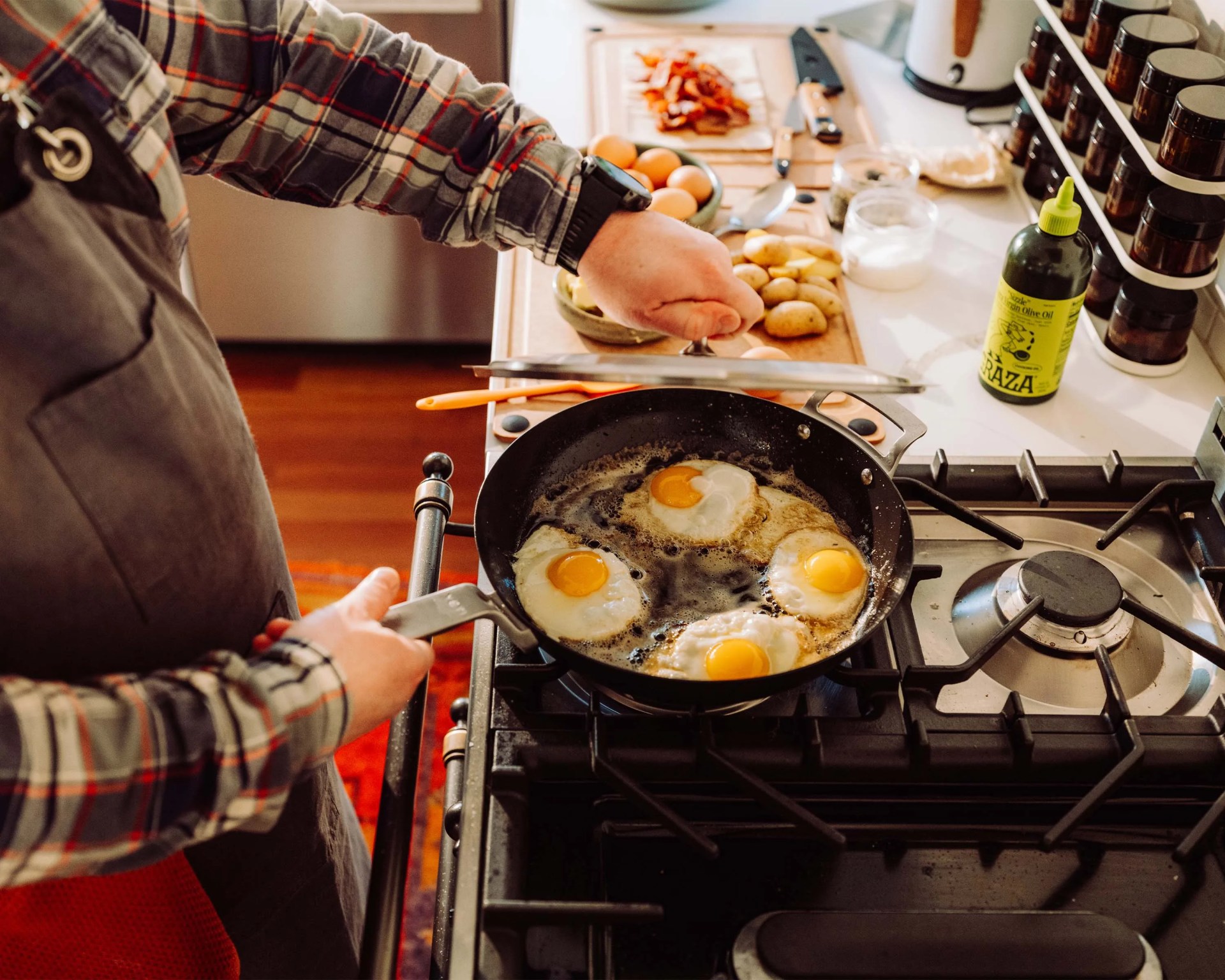 Person lifting the lid off a frying pan with four eggs cooking on a gas stove.