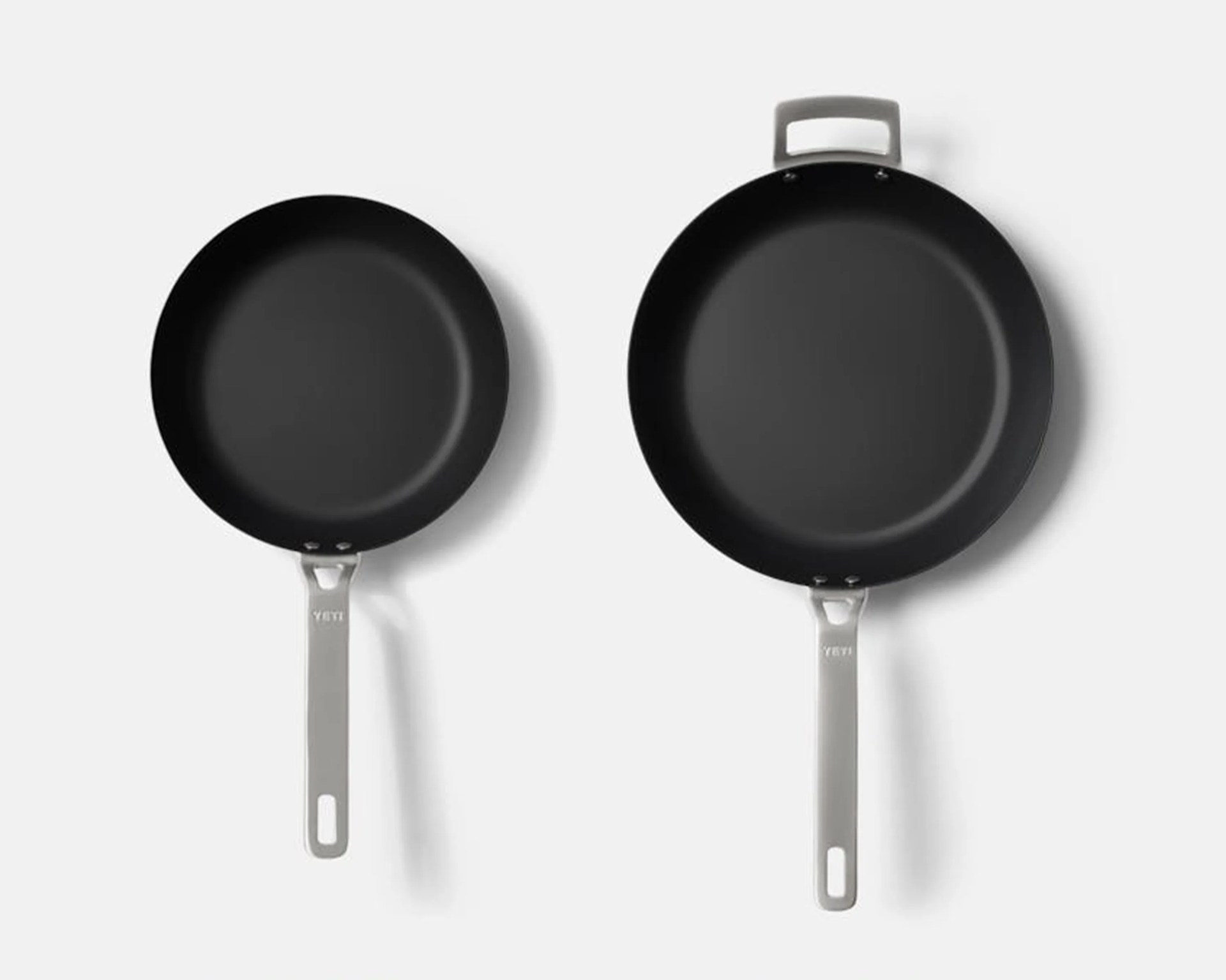 Two black frying pans with gray handles, one smaller and one larger with an additional loop handle, on a white background.