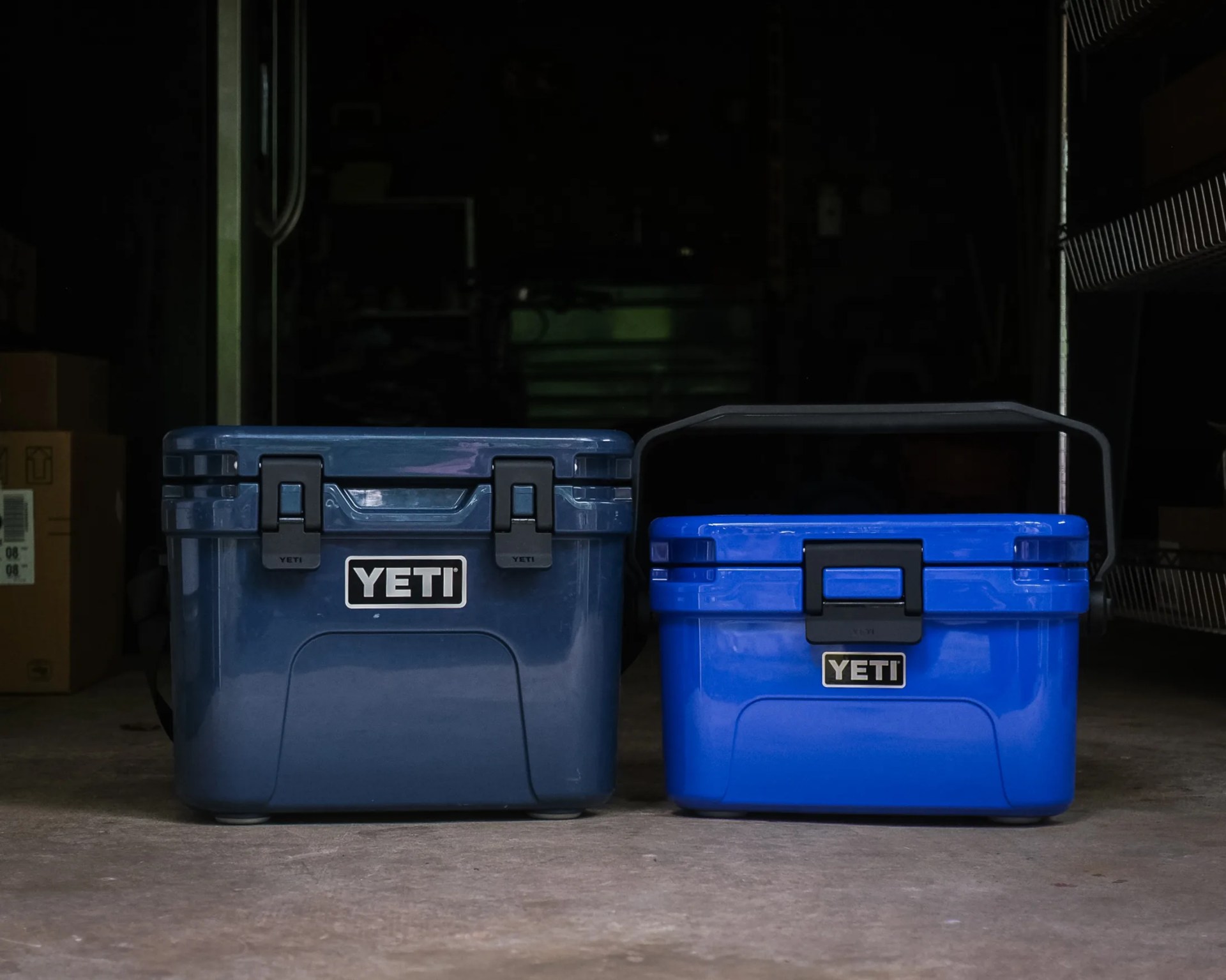 Two YETI coolers, one dark blue and one bright blue with a black handle, placed on a concrete floor.