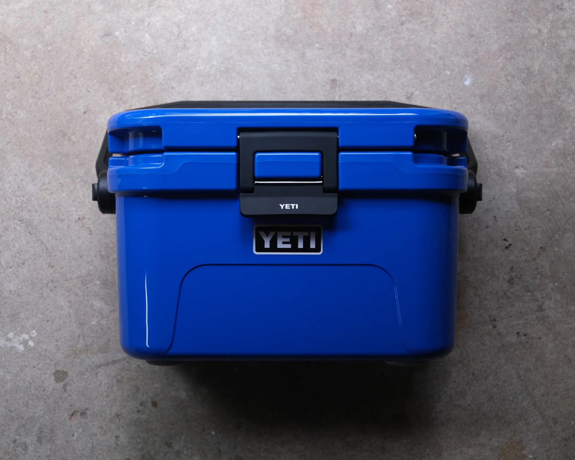 Blue YETI cooler with black latch on a concrete surface.