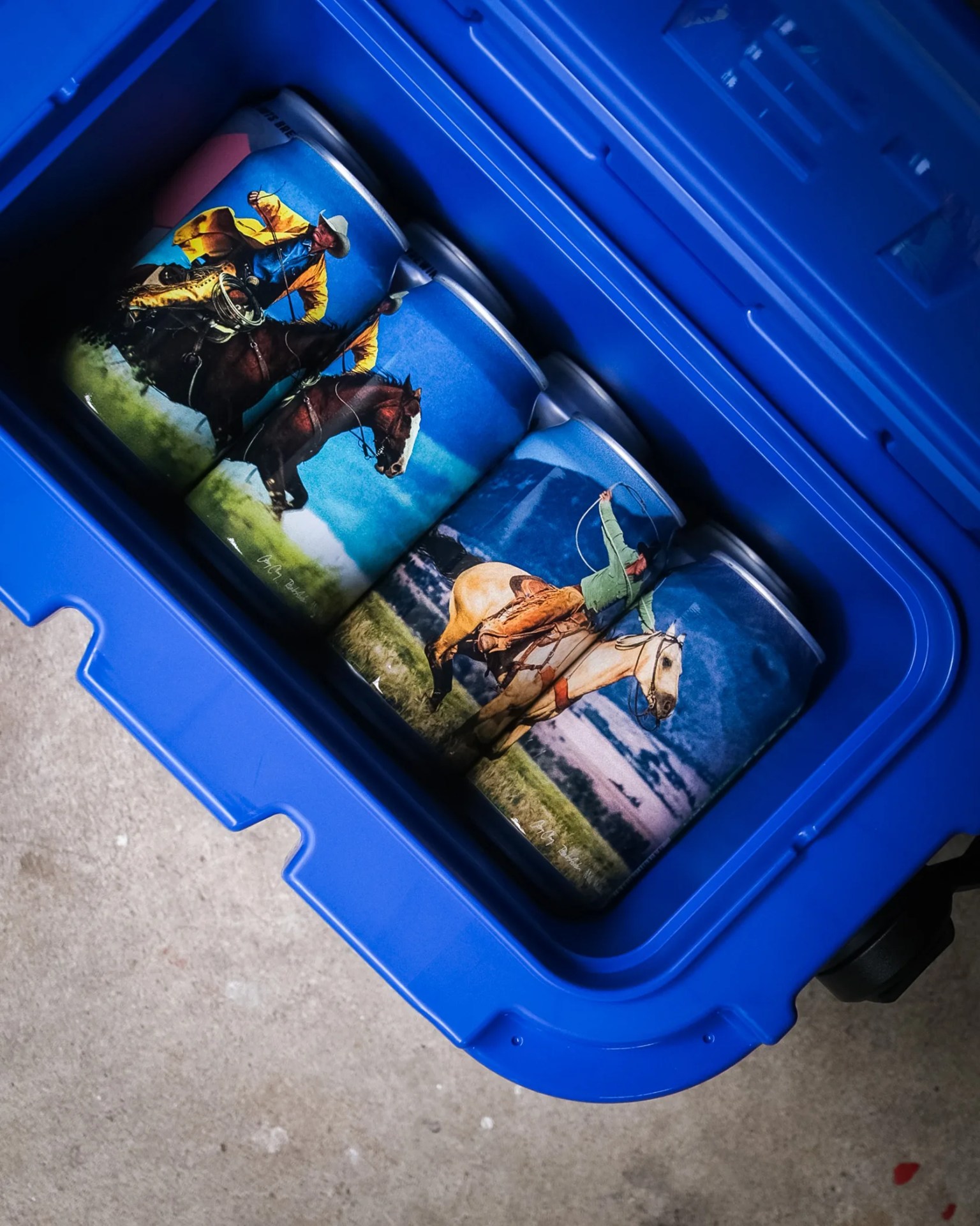 Blue cooler with cans featuring cowboy and horse illustrations inside.