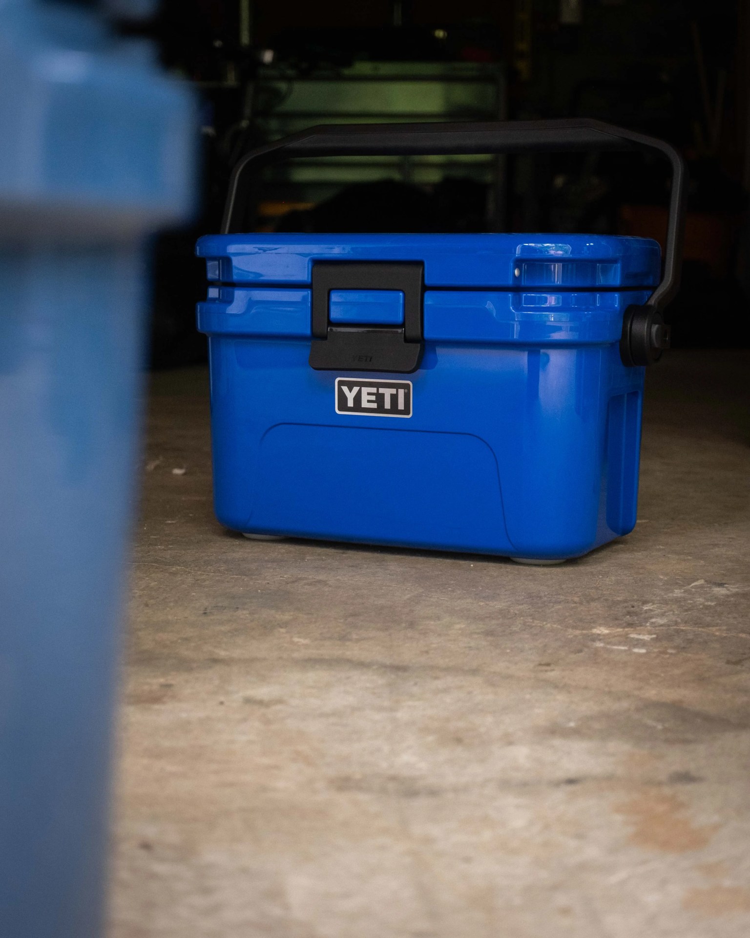 Blue YETI cooler with black handle on a concrete floor in a dimly lit space.