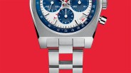 Close-up of a silver metal wristwatch with blue and white dial, red second hand, and date window showing the number 4 on a red background.