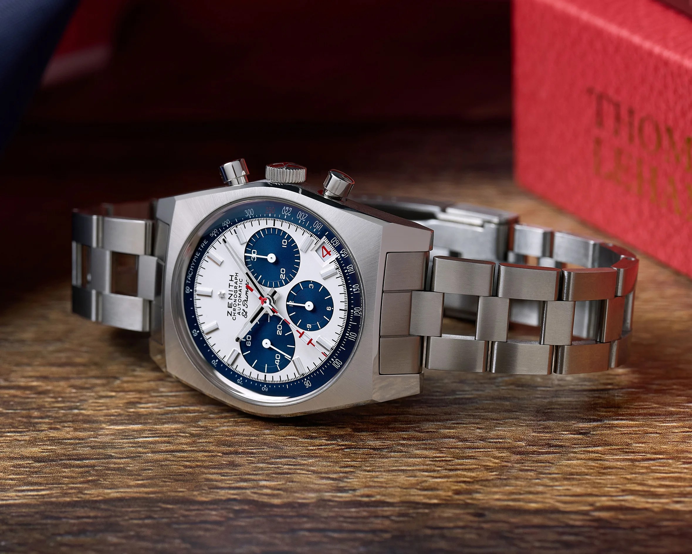 Stainless steel Zenith chronograph wristwatch with white dial and blue subdials on a wooden surface.