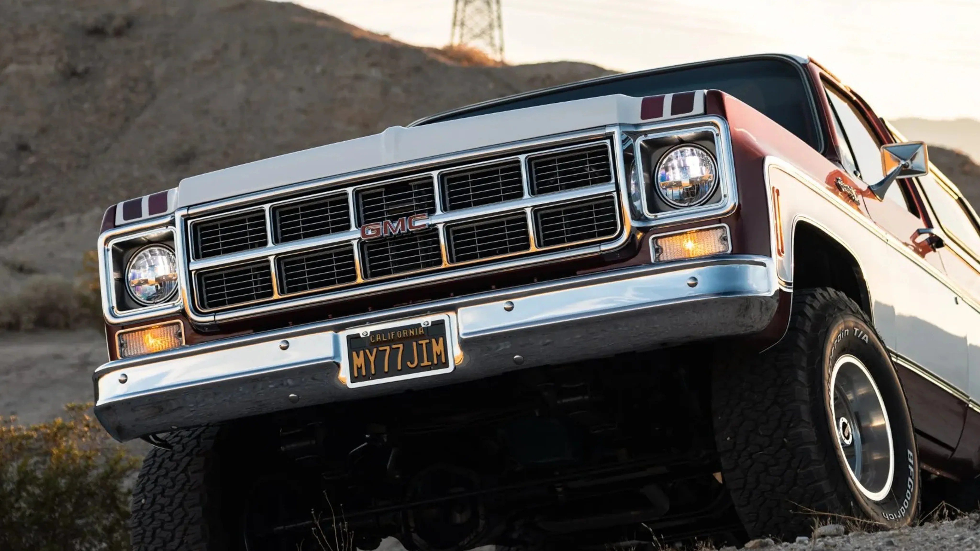 Front view of a vintage maroon and white GMC truck with California license plate MY77JIM on a rocky terrain.