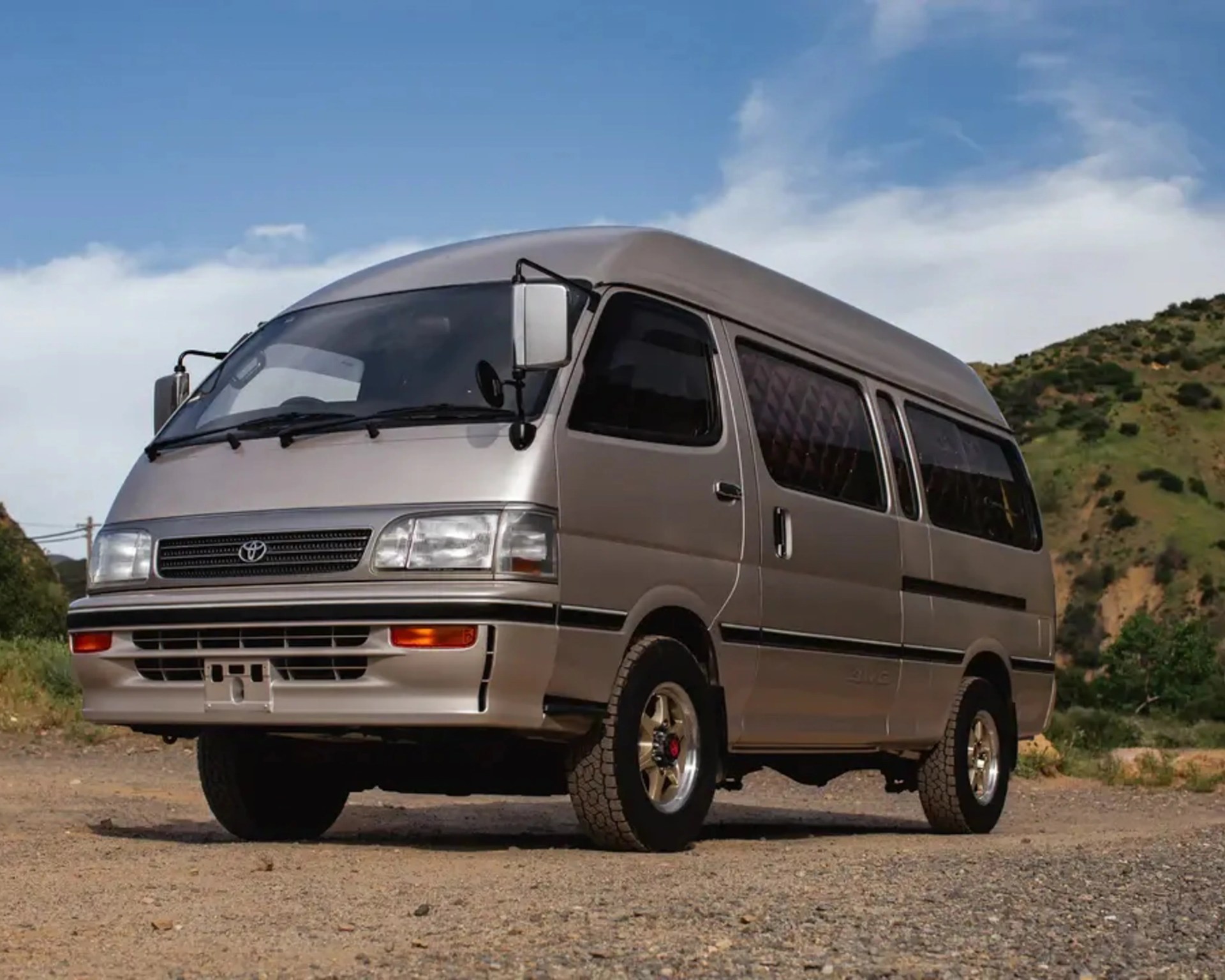 Silver Toyota van with tinted windows parked on a gravel road with hills in the background.