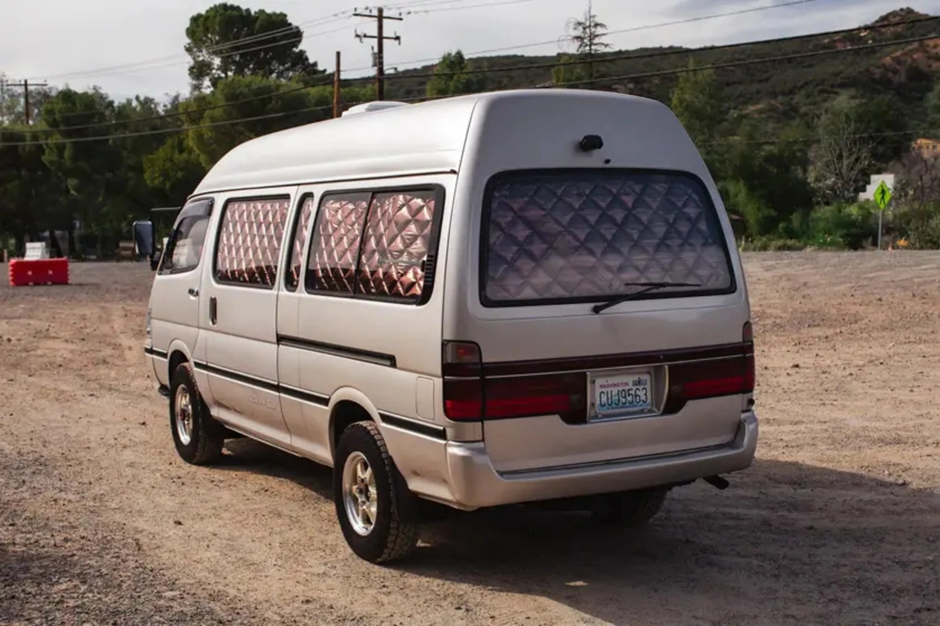 White camper van with quilted reflective window covers parked on a dirt road.