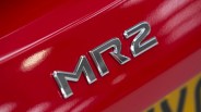 Chrome "MR2" badge on a shiny red car surface with part of a yellow license plate visible.