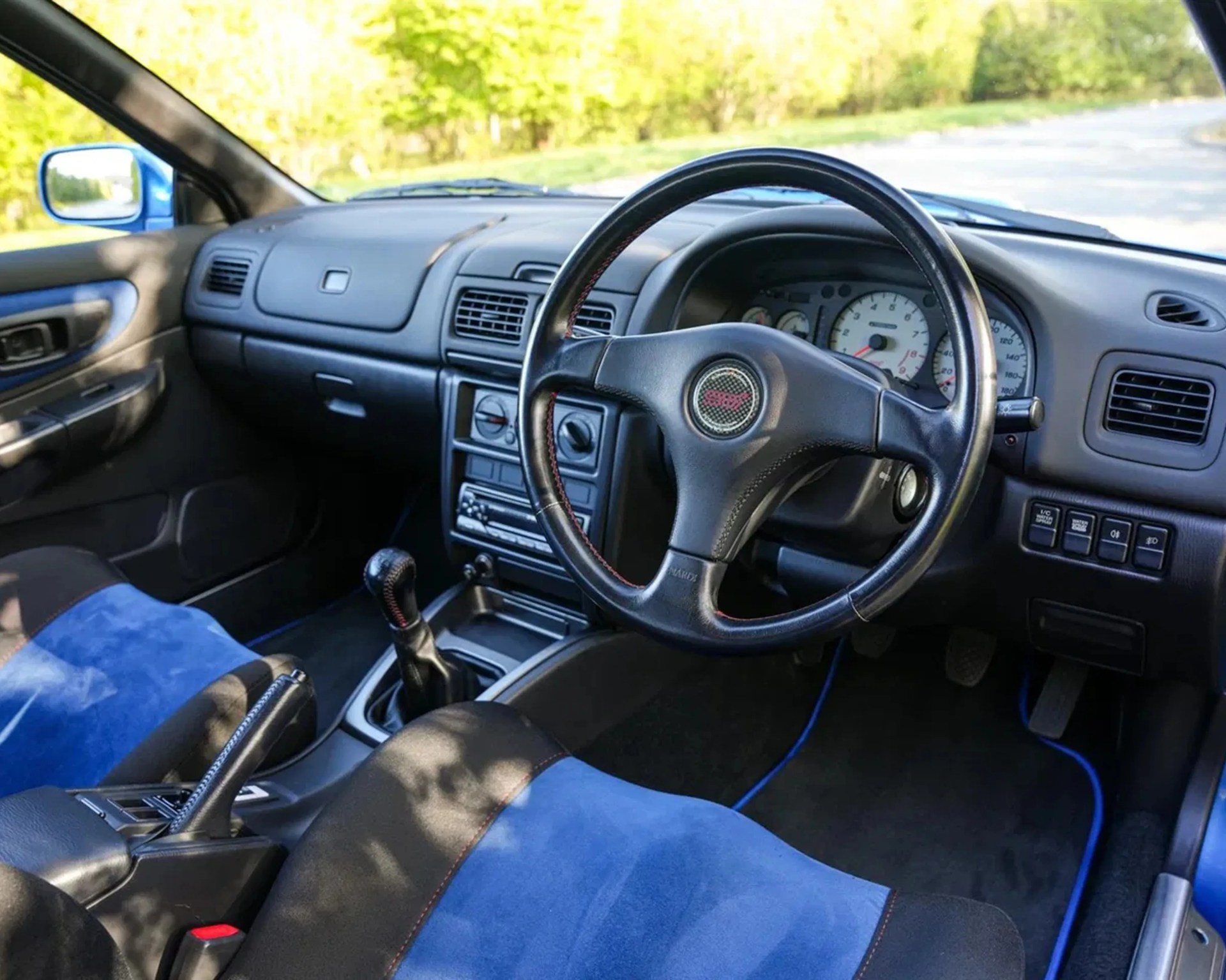 Black and blue suede car seats with a black leather steering wheel featuring a red STI logo.