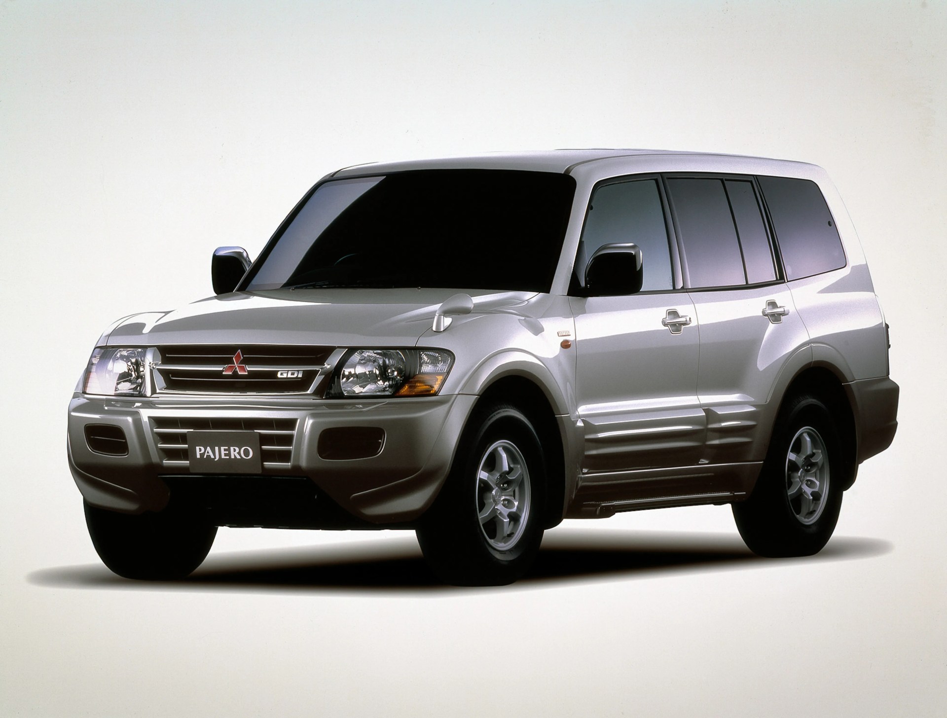 Silver Mitsubishi Pajero SUV with tinted windows and black side mirrors on a white background.