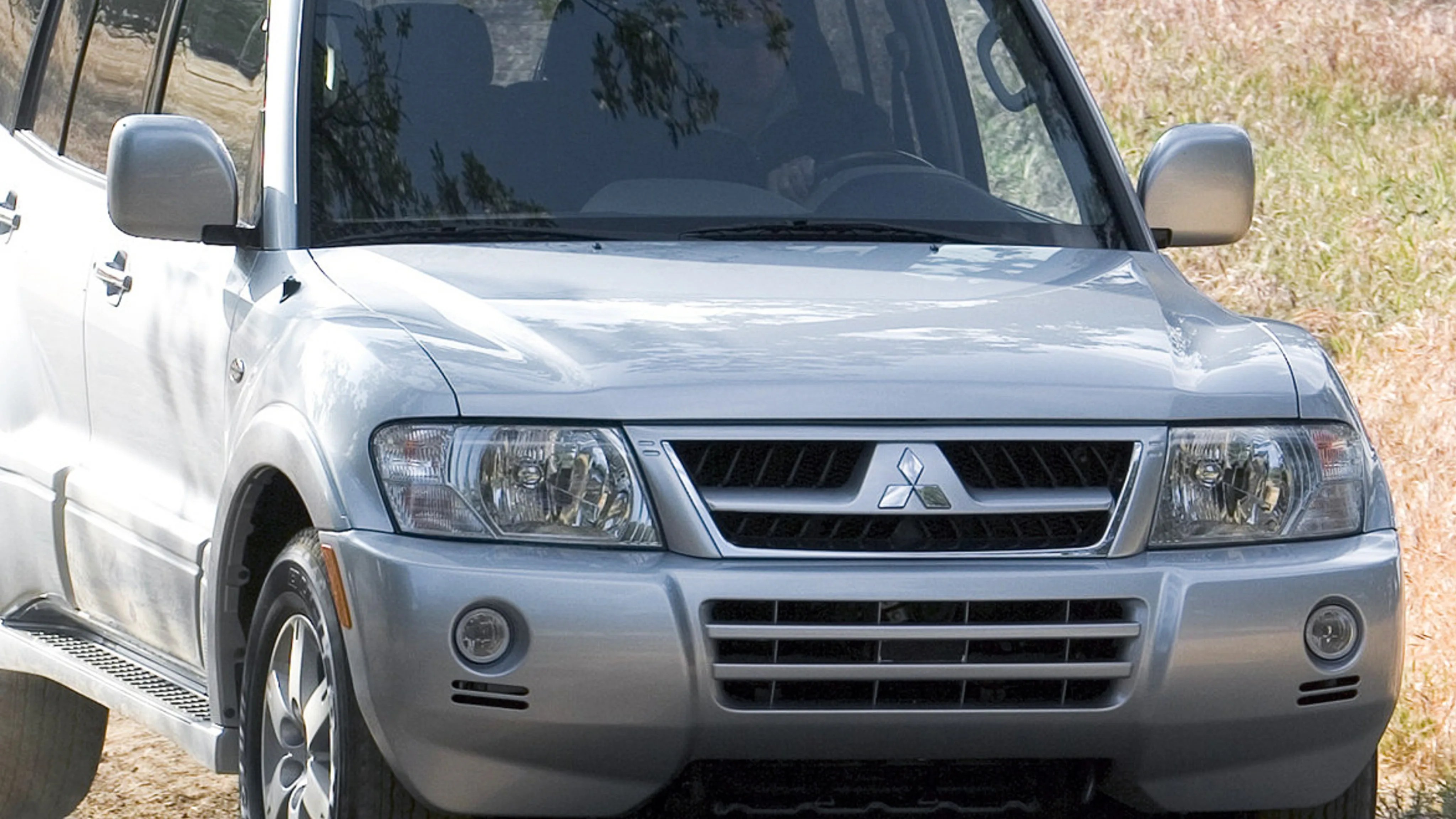 Silver Mitsubishi SUV front view with visible grille and headlights on a dirt road.