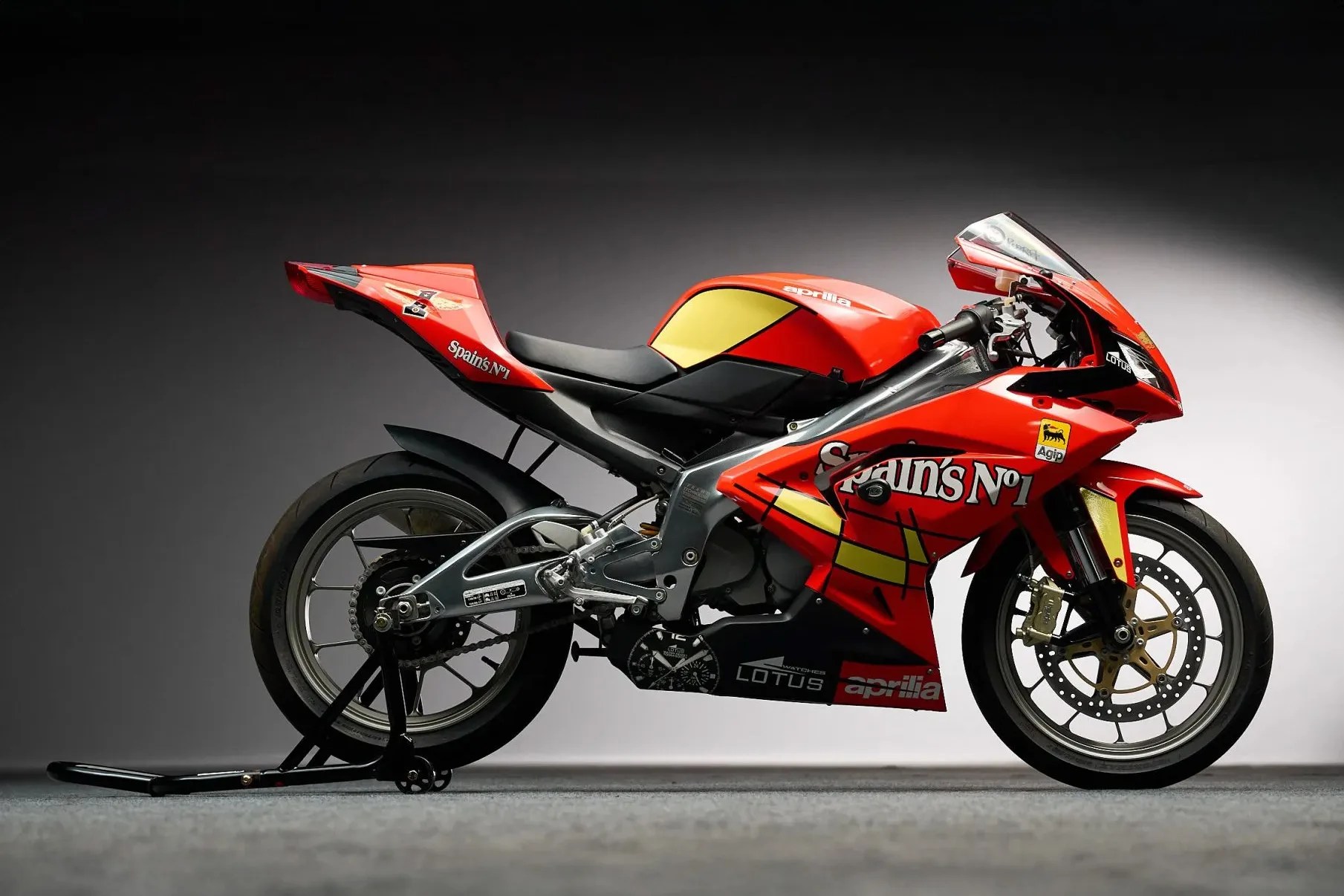 Red and yellow Aprilia racing motorcycle with "Spain's No 1" decals on a stand.