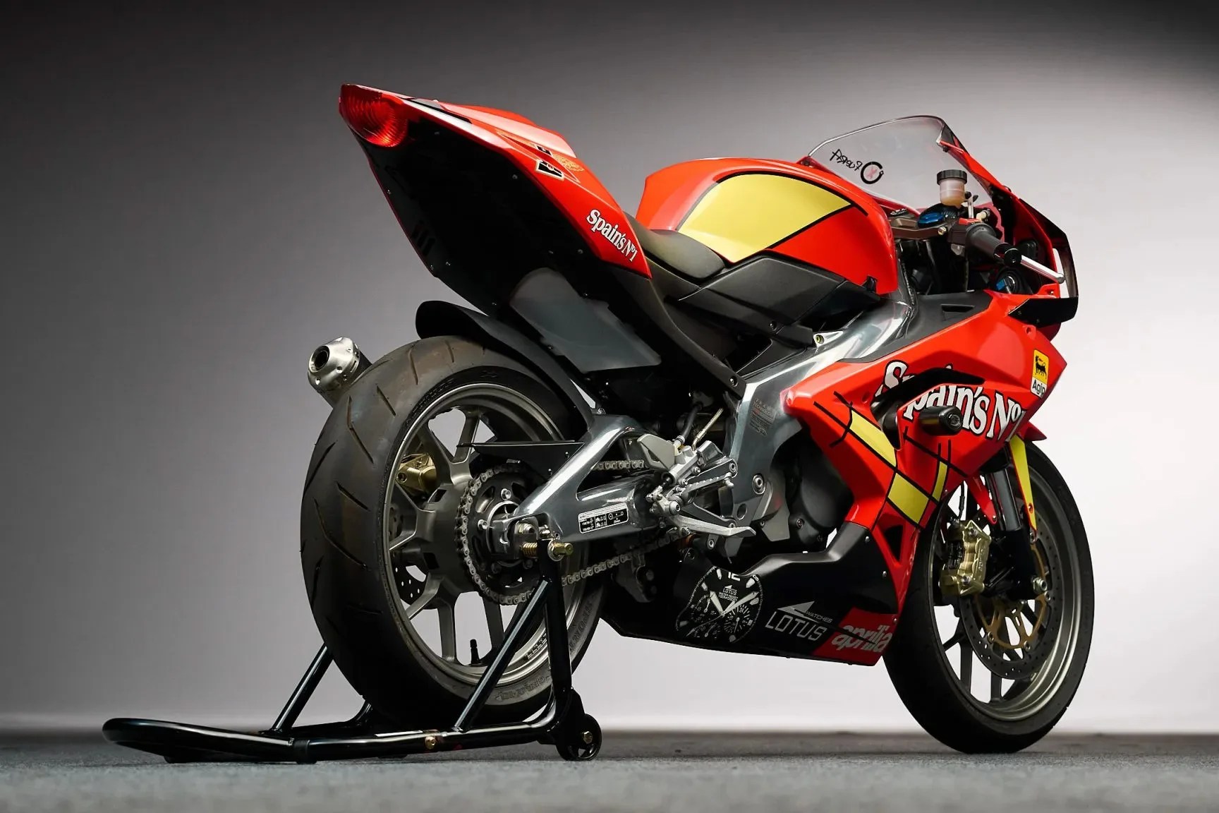 Red and yellow racing motorcycle with Spain's No.1 decals on a rear stand against a gray background.