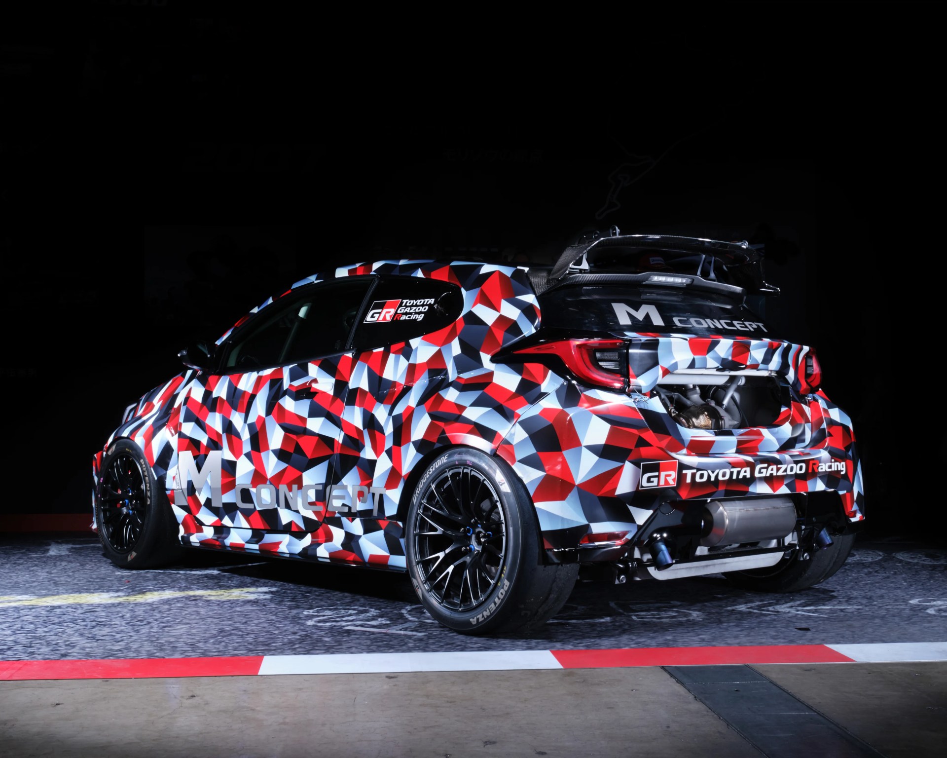 Toyota Gazoo Racing M Concept car with red, white, and black geometric camouflage and large rear spoiler.