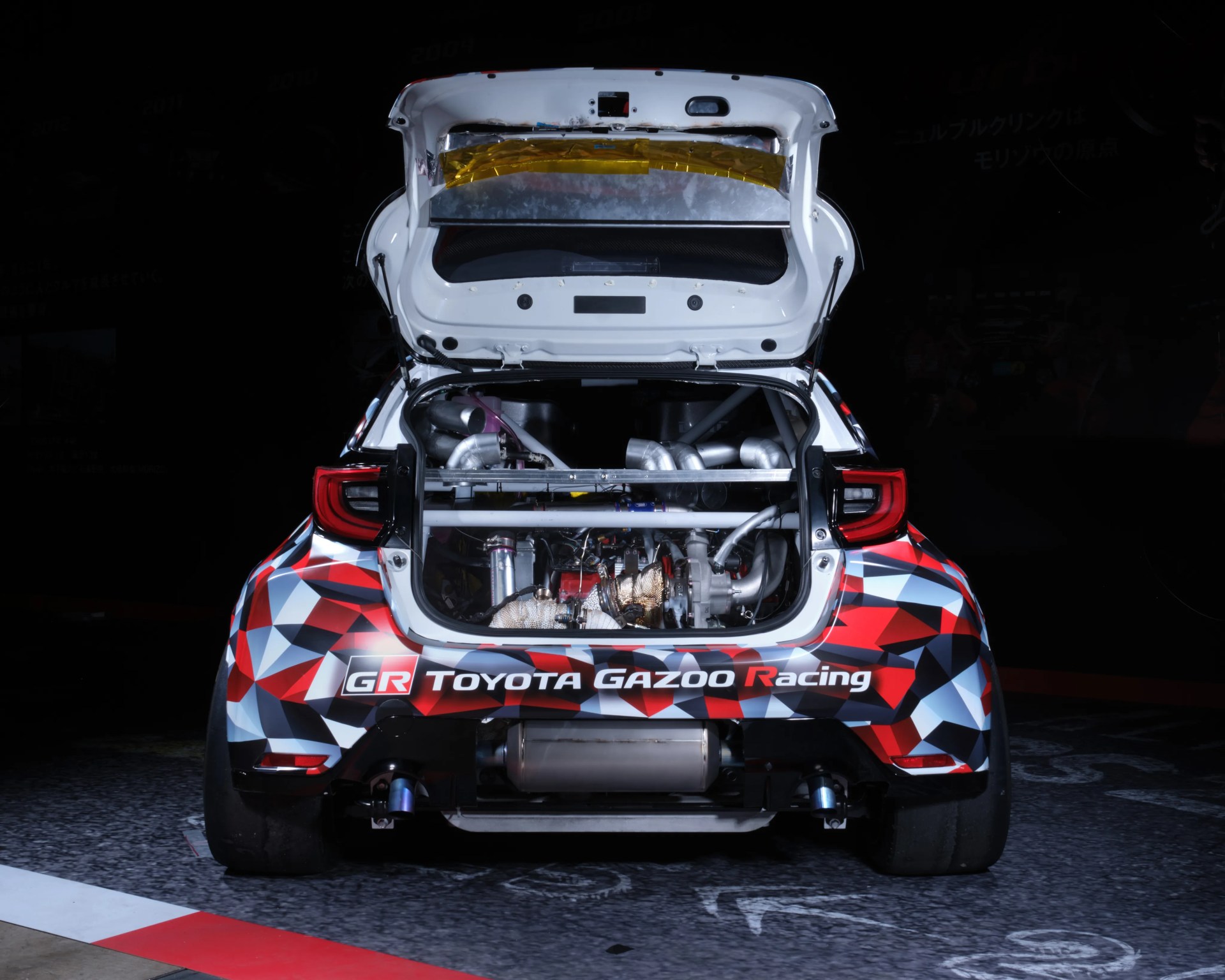 Rear view of a Toyota Gazoo Racing car with open engine compartment showing exhaust pipes and turbo components.