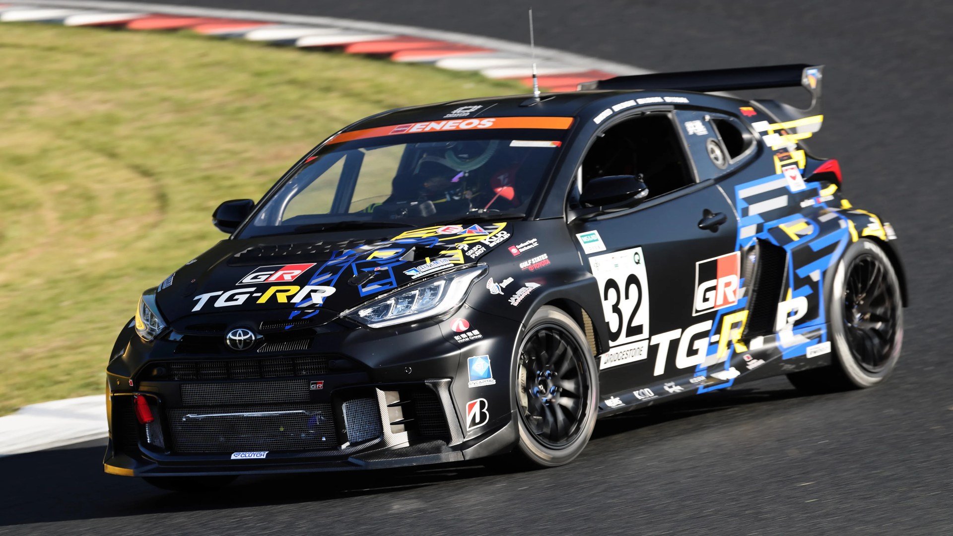 Black Toyota GR race car with blue and yellow graphics and number 32 on a racetrack.