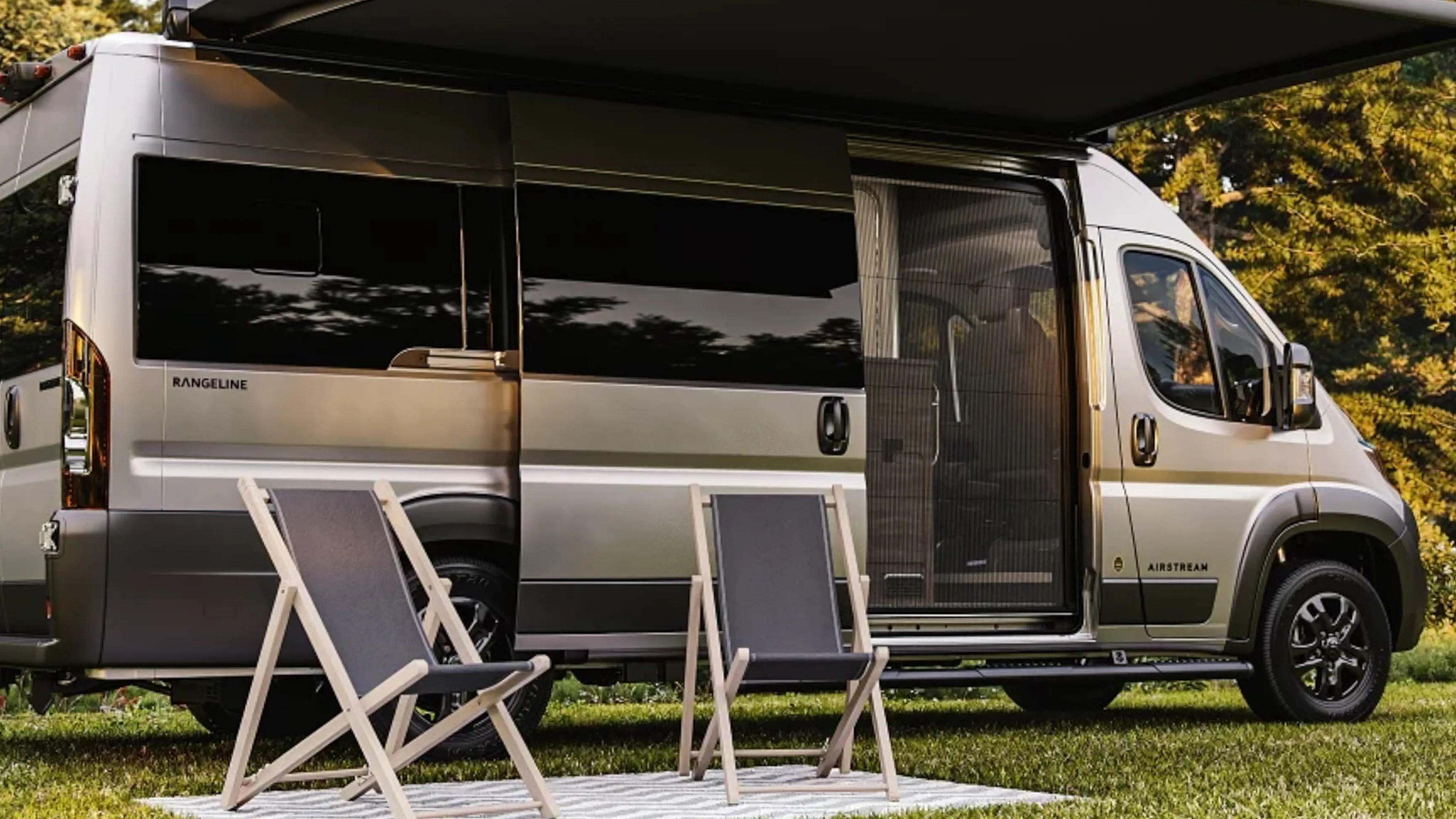 Silver Airstream Rangeline camper van with sliding door open and two folding chairs on a striped rug outside.