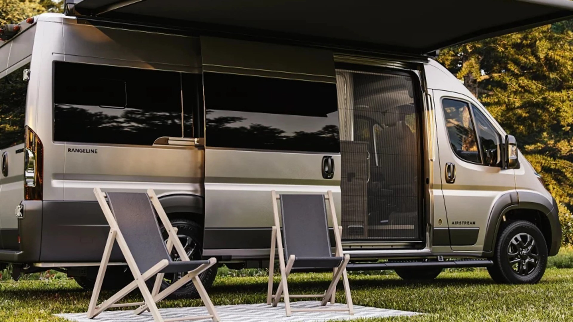 Silver Airstream Rangeline camper van with sliding door open and two folding chairs on a striped rug outside.