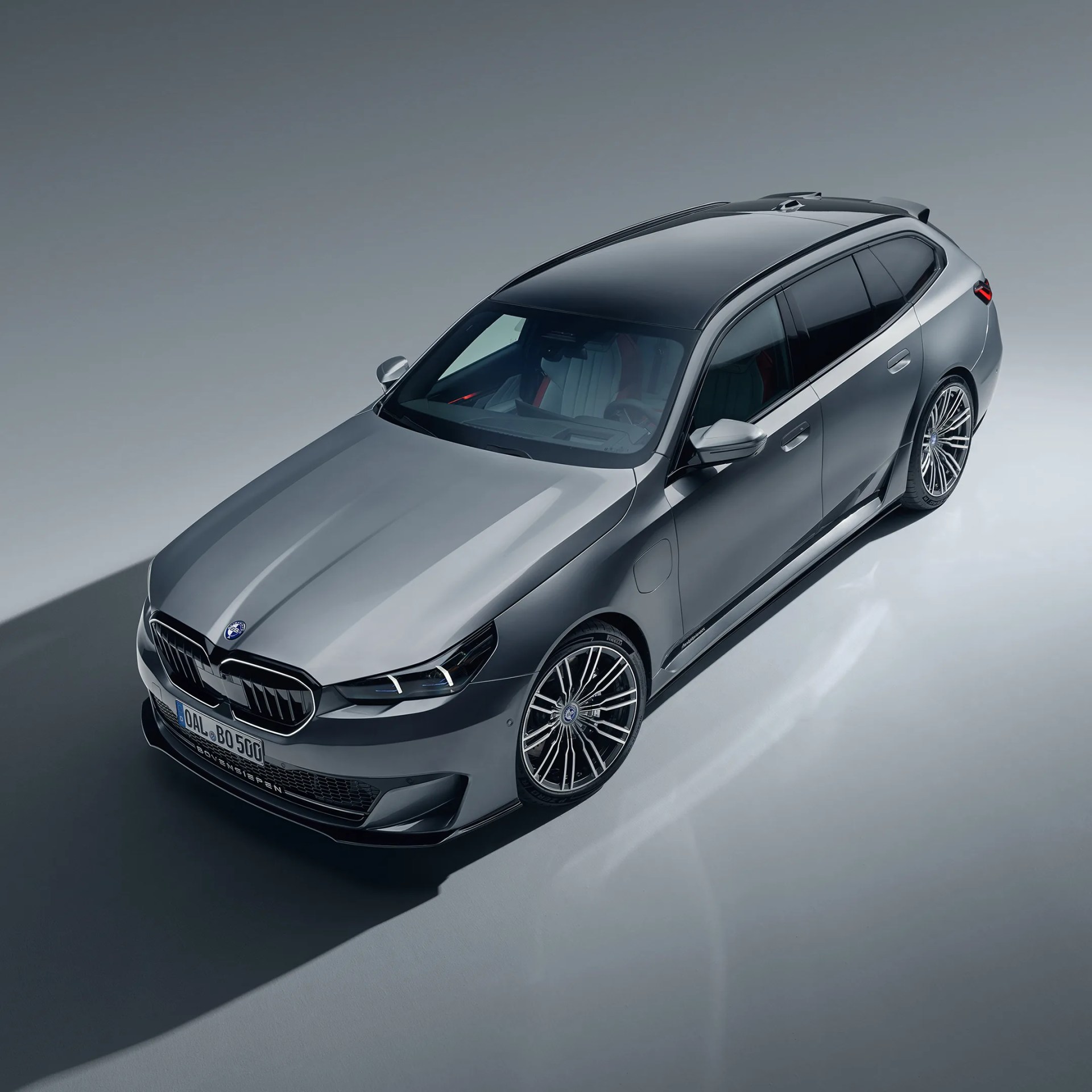 Silver luxury station wagon with black roof and multi-spoke alloy wheels on a gray surface.