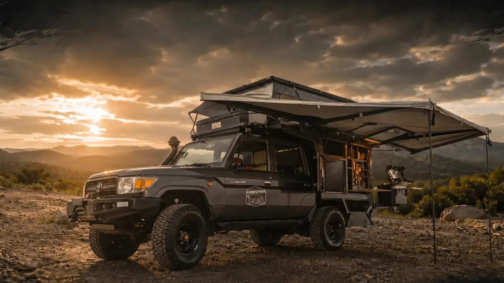 Black Toyota Land Cruiser with rooftop tent and extended awning set up on rocky terrain at sunset.