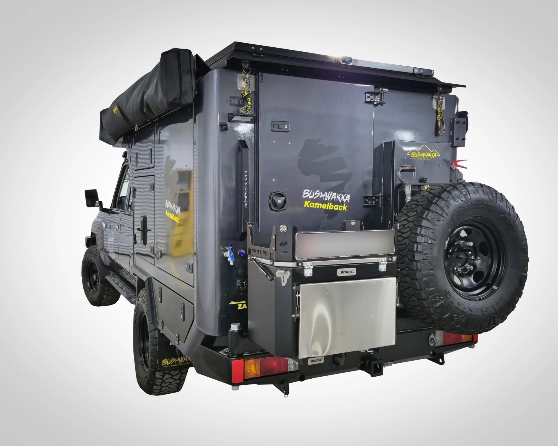 Black Bushwakka Kamelback off-road camper vehicle with spare tire and rooftop storage bag.