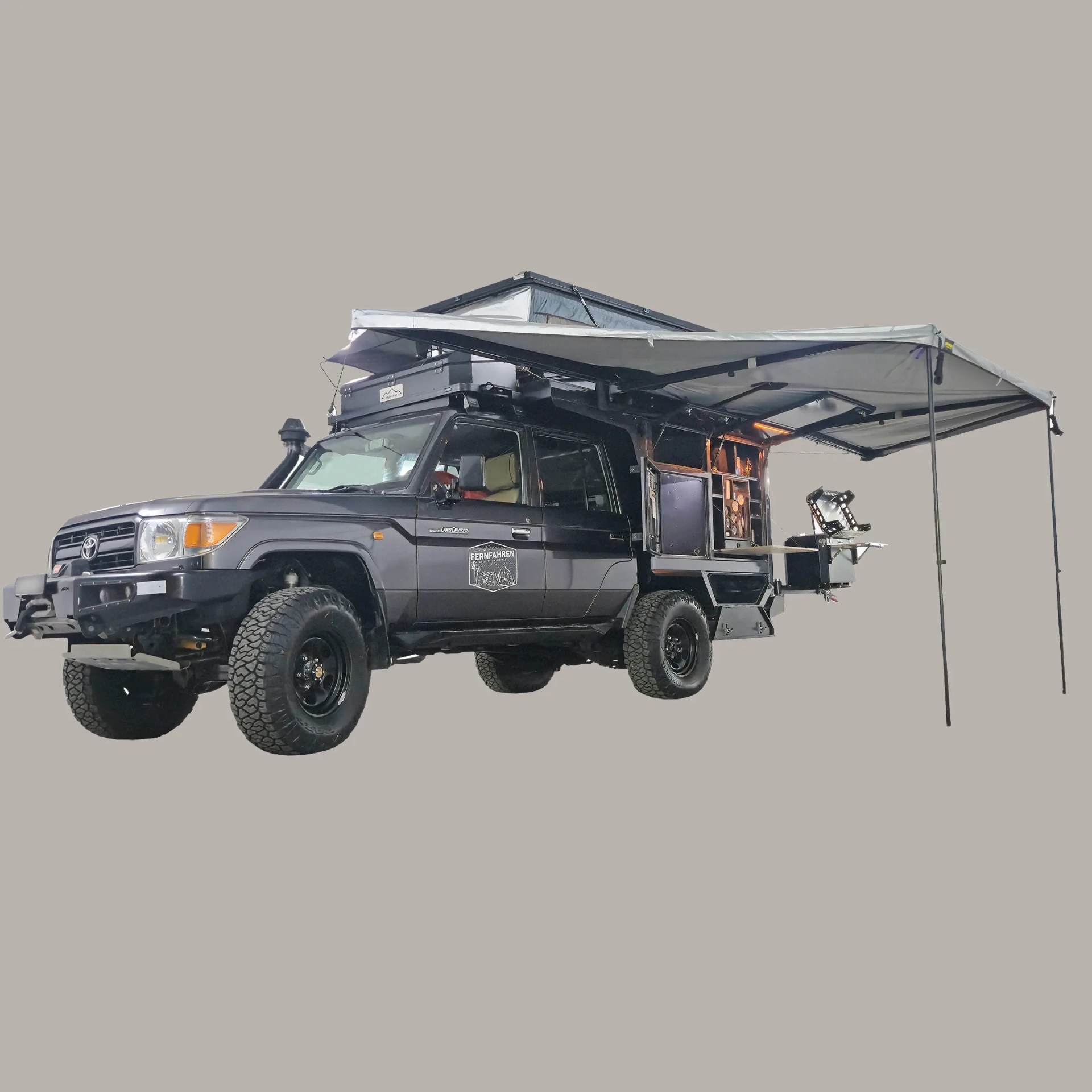 Black Toyota Land Cruiser camper truck with rooftop tent and extended side awning.