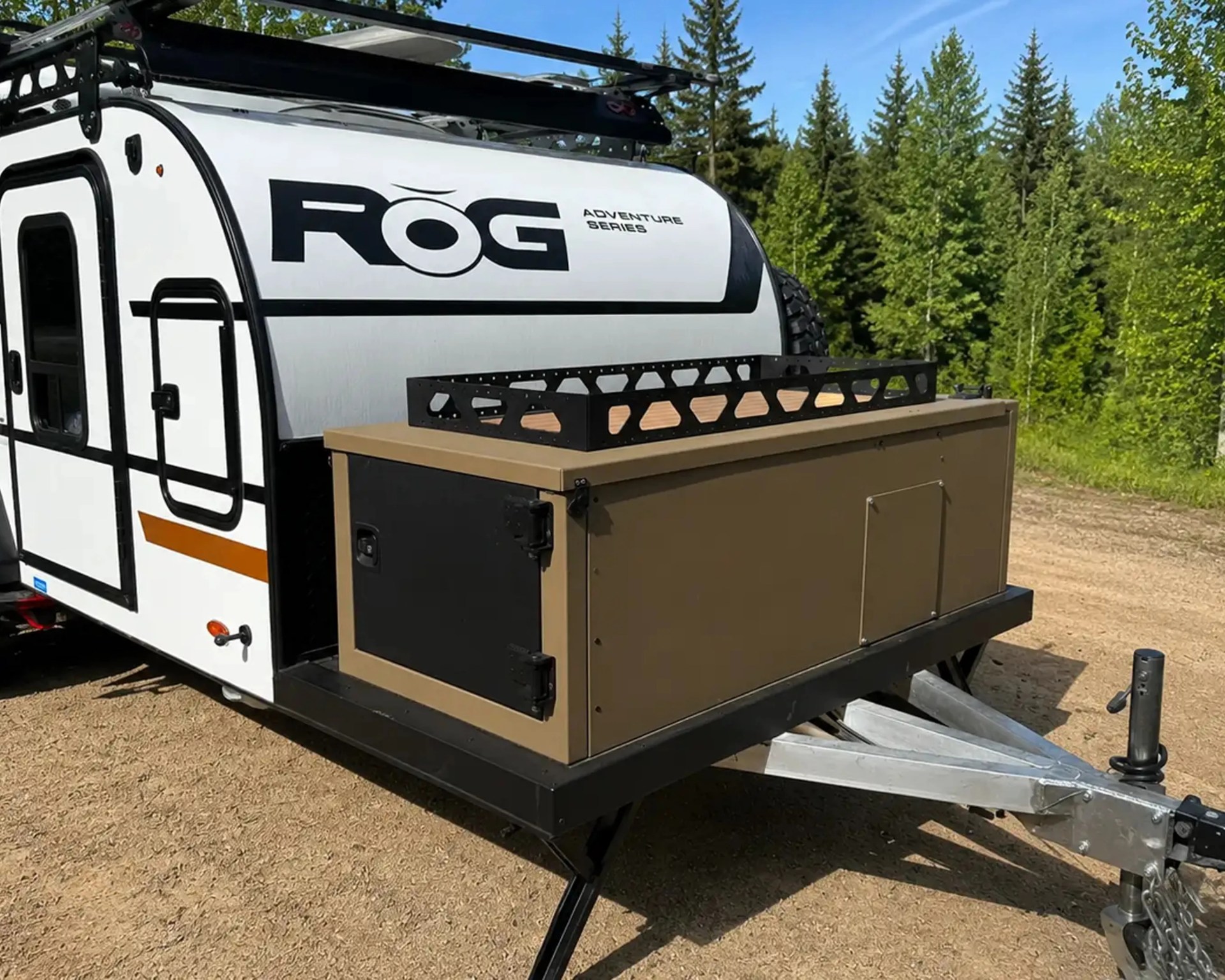 White ROG Adventure Series camper trailer with black trim and attached brown storage box on a trailer hitch.
