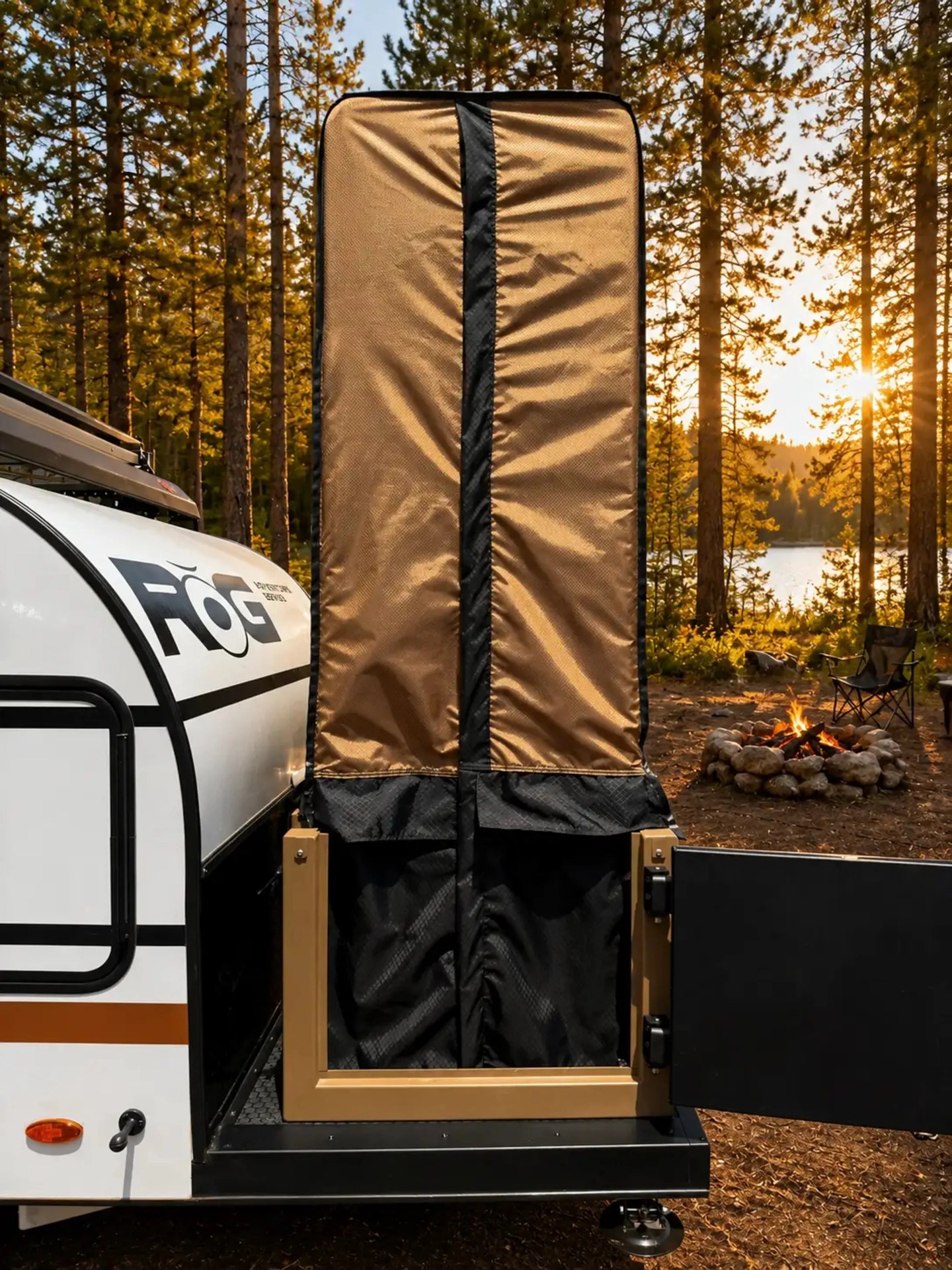 Brown and black protective cover mounted on the back of a white ROG camper trailer near a campfire in a forest.