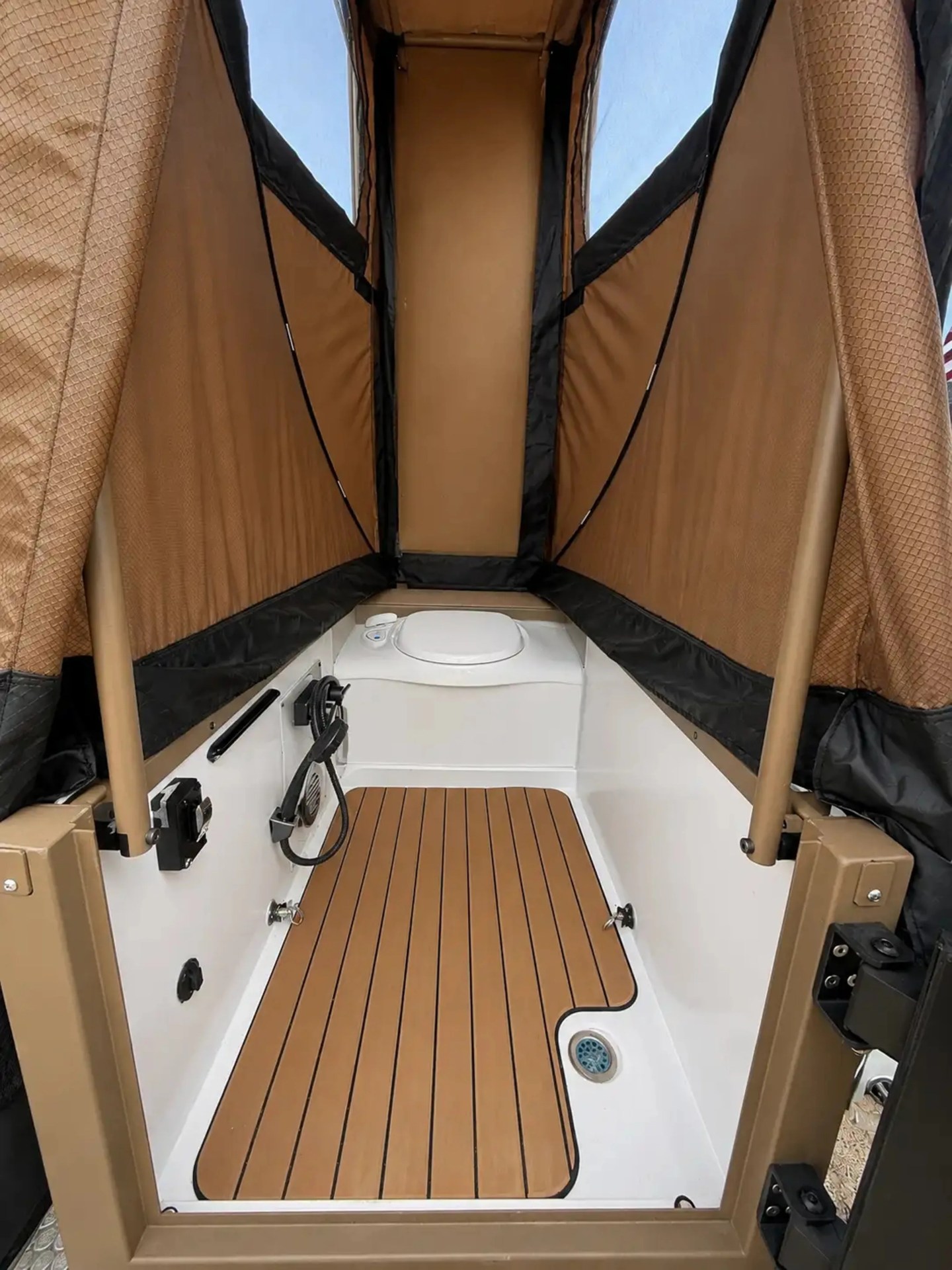Compact marine toilet area with brown cushioned floor mat and tan privacy curtains.