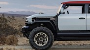 Front side view of a white off-road vehicle with a red roof and large rugged tires in a desert landscape.