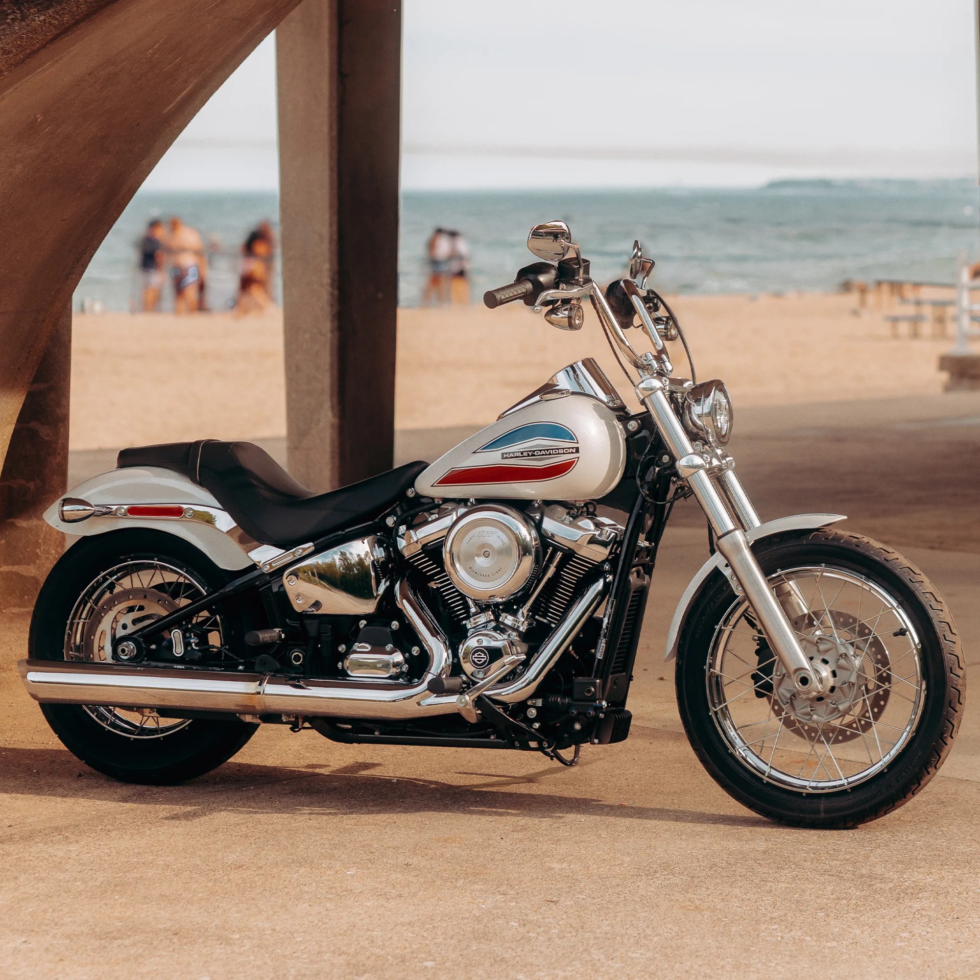 White Harley-Davidson motorcycle with chrome details parked on a sandy beach near wooden pillars.