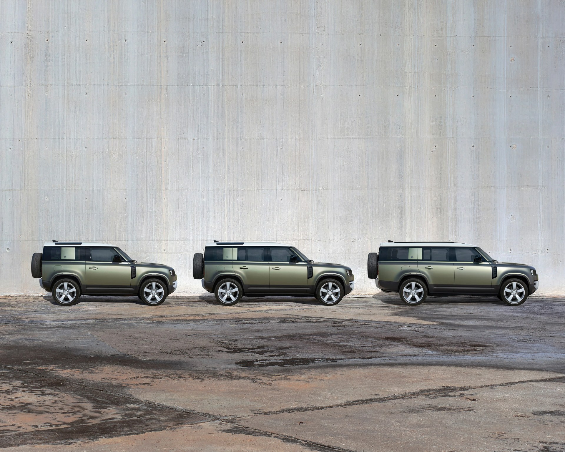 Three olive green SUVs with white roofs parked side by side against a large concrete wall.