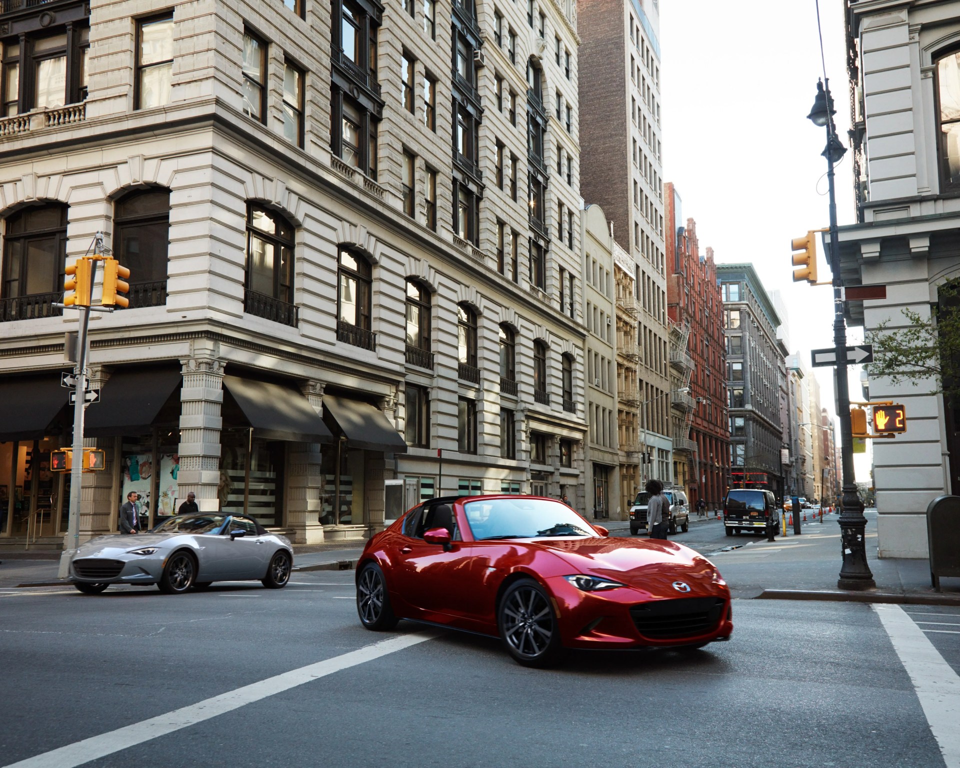 Red Mazda convertible sports car and silver convertible sports car on city street with historic buildings.