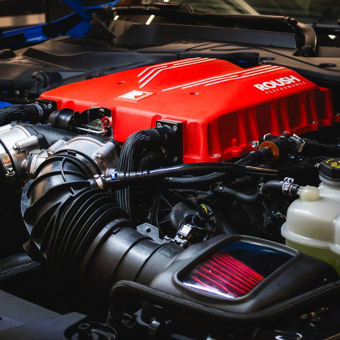Close-up of a car engine featuring a red ROUSH Performance cover and black intake components.
