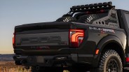 Black Ford F-150 Shelby Raptor pickup truck rear with off-road tires and roof light bar at sunset.