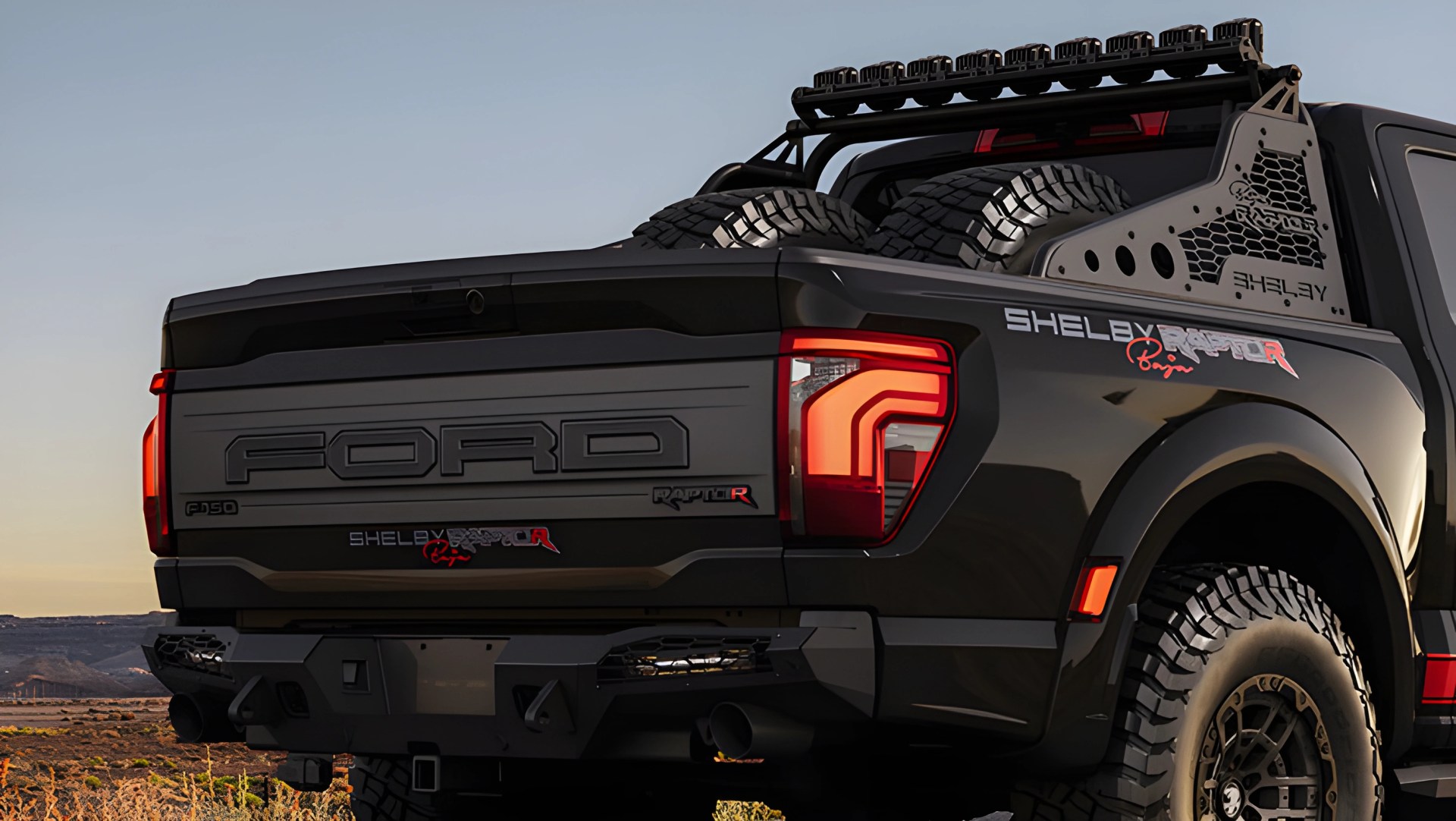 Black Ford F-150 Shelby Raptor pickup truck rear with off-road tires and roof light bar at sunset.