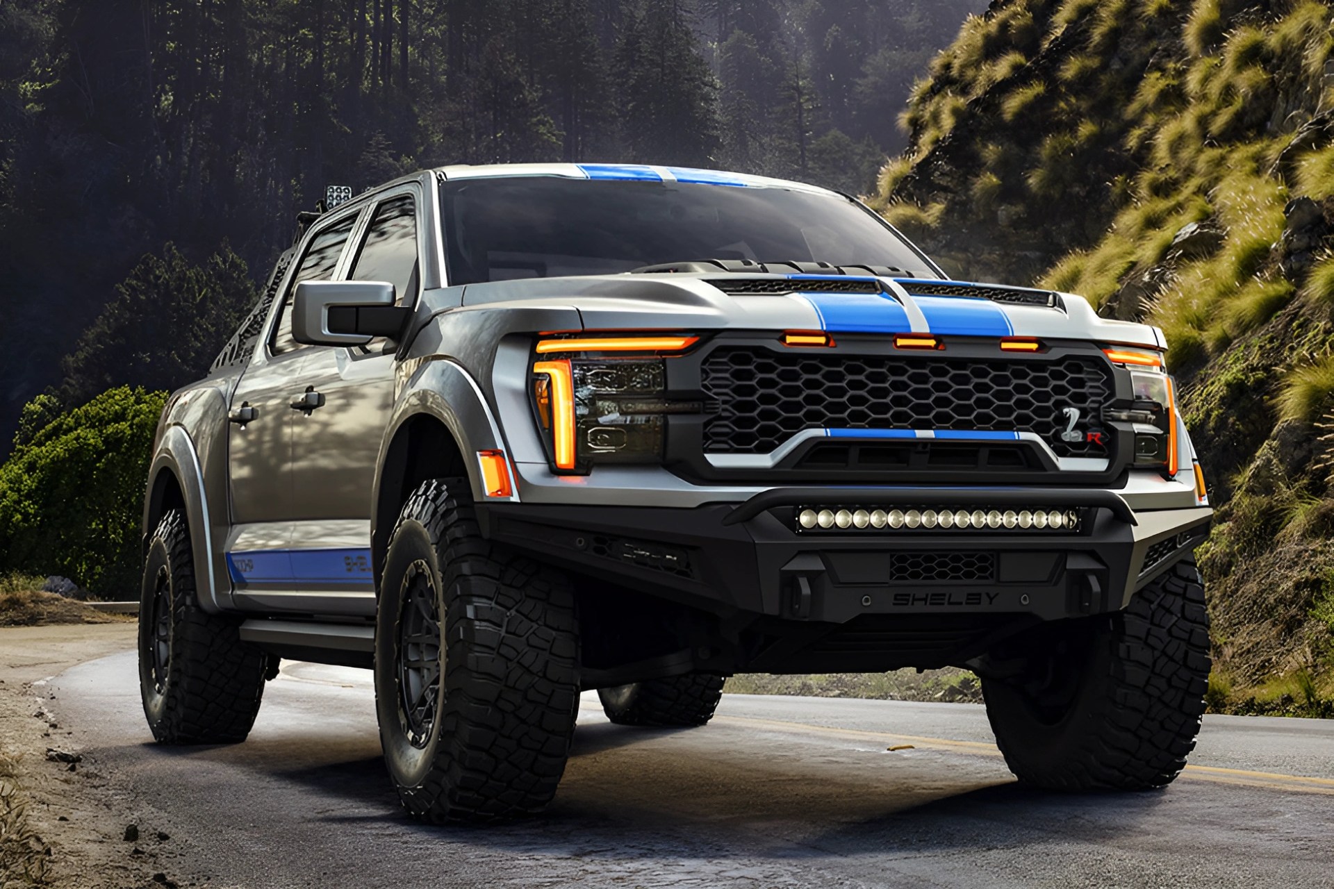 Silver and blue Shelby off-road pickup truck with large tires on a mountain road.