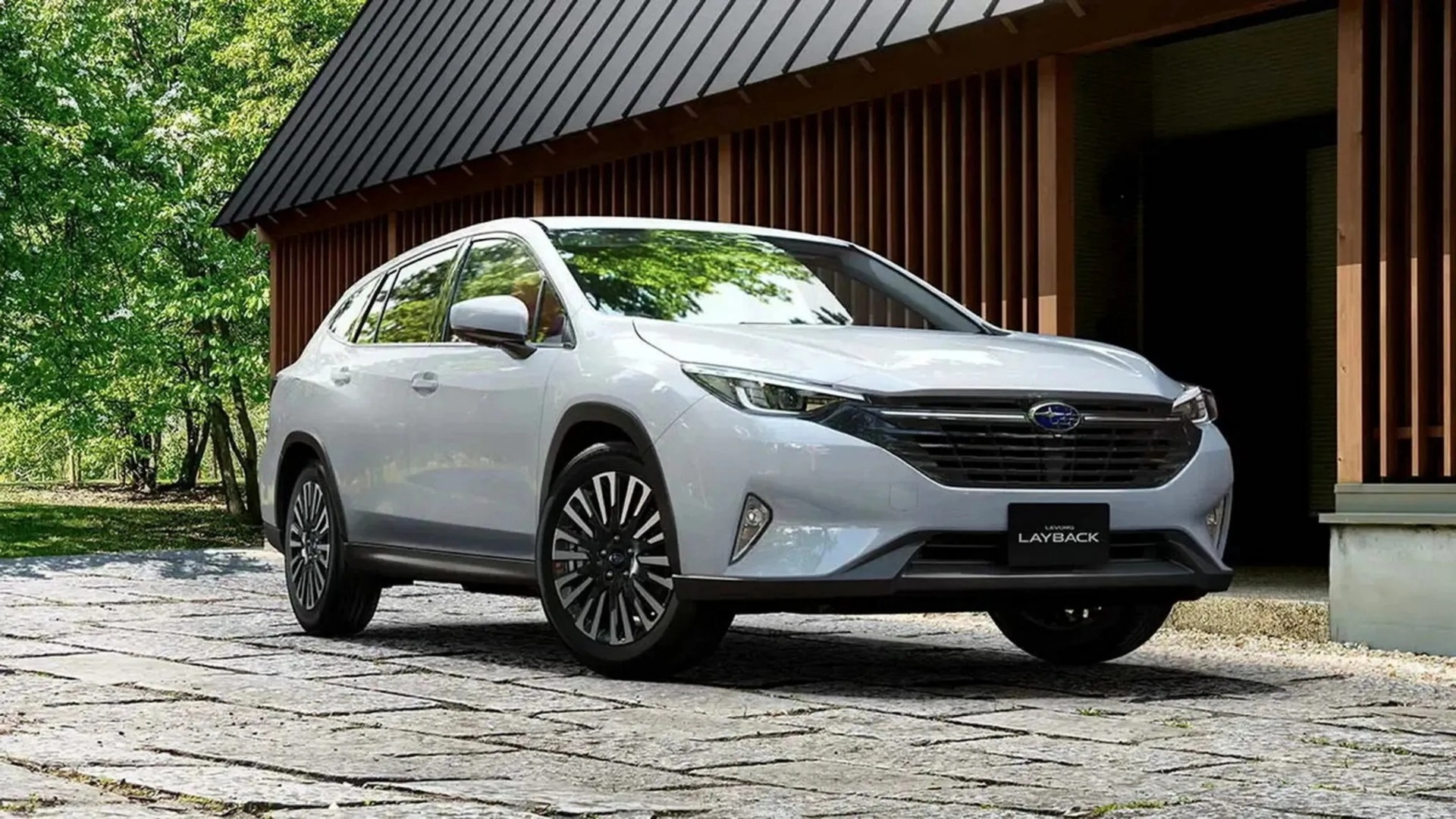 White Subaru Layback SUV parked on stone pavement in front of a modern wooden building with trees in the background.