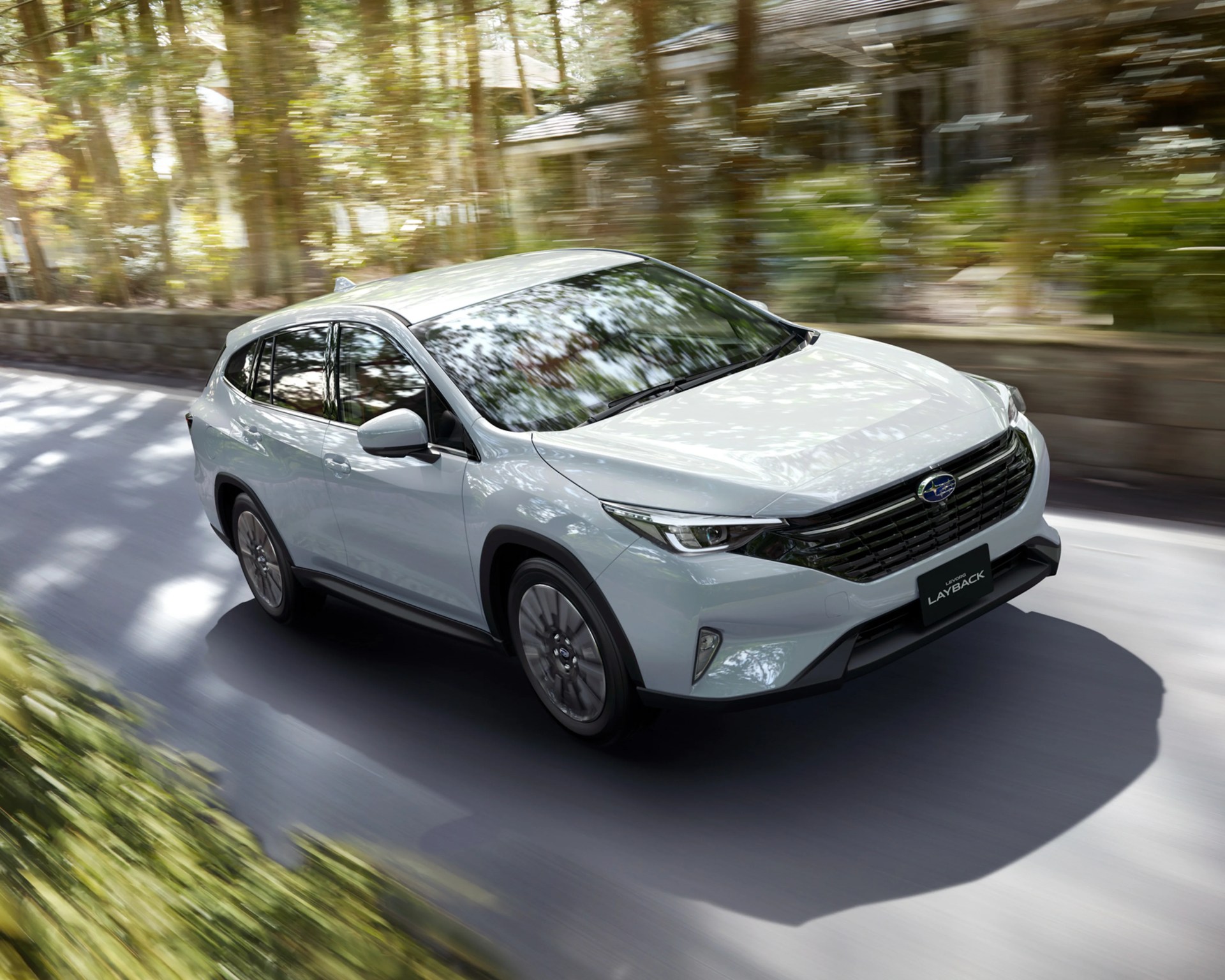 Silver Subaru SUV driving on a shaded road with trees reflected on the windshield.