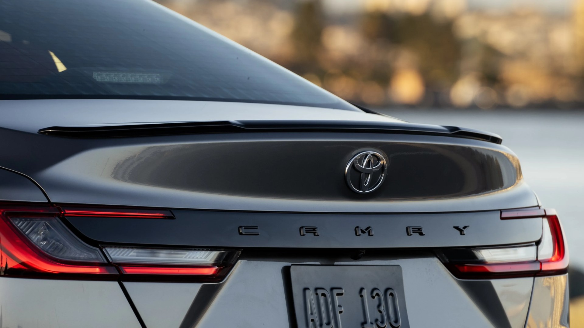 Rear view of a gray Toyota Camry with illuminated taillights and a visible license plate.